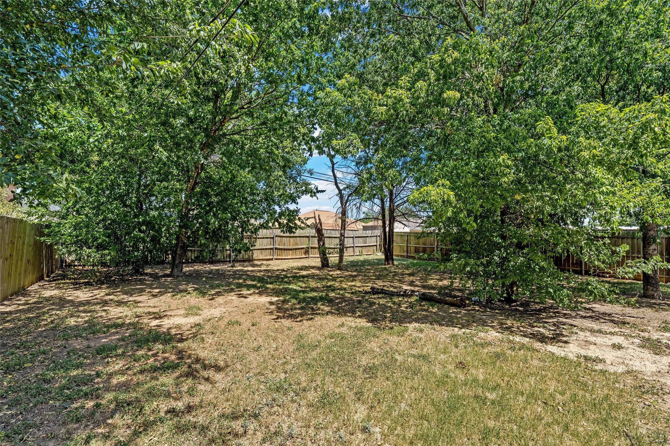Expansive outdoor space featuring mature trees and a perimeter privacy fence