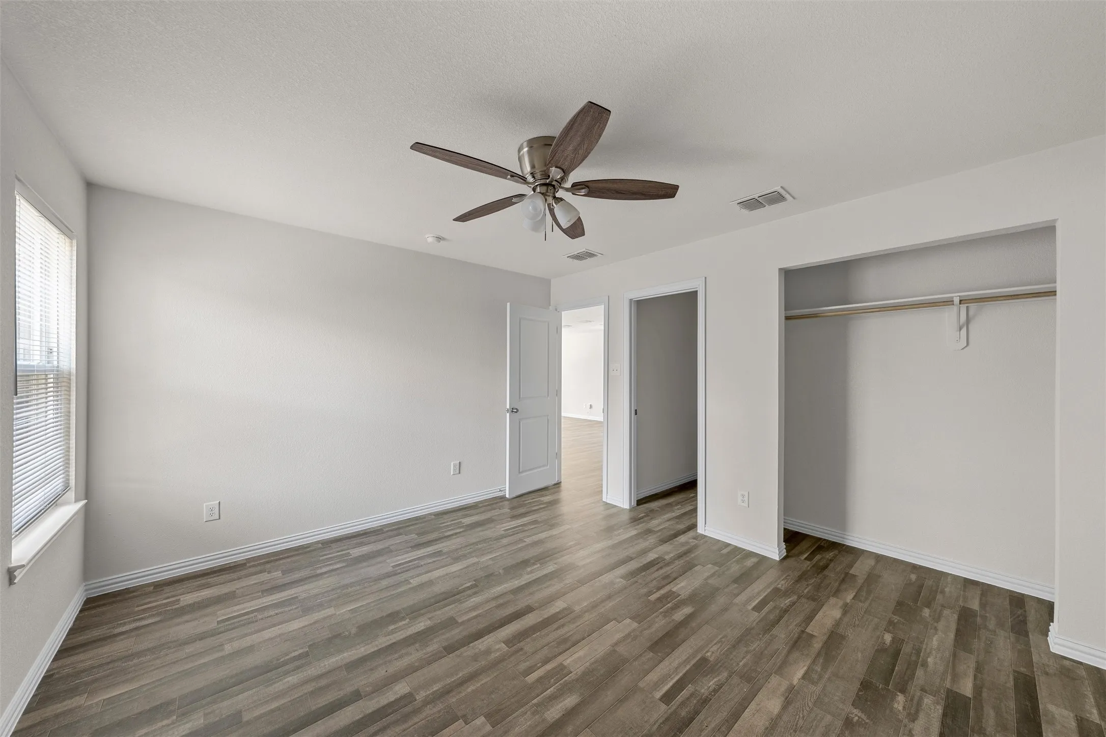 Spacious bedroom featuring wood-finish flooring, ceiling fan with integrated lighting, large closet with rod and shelf storage, and abundant natural light from multiple windows