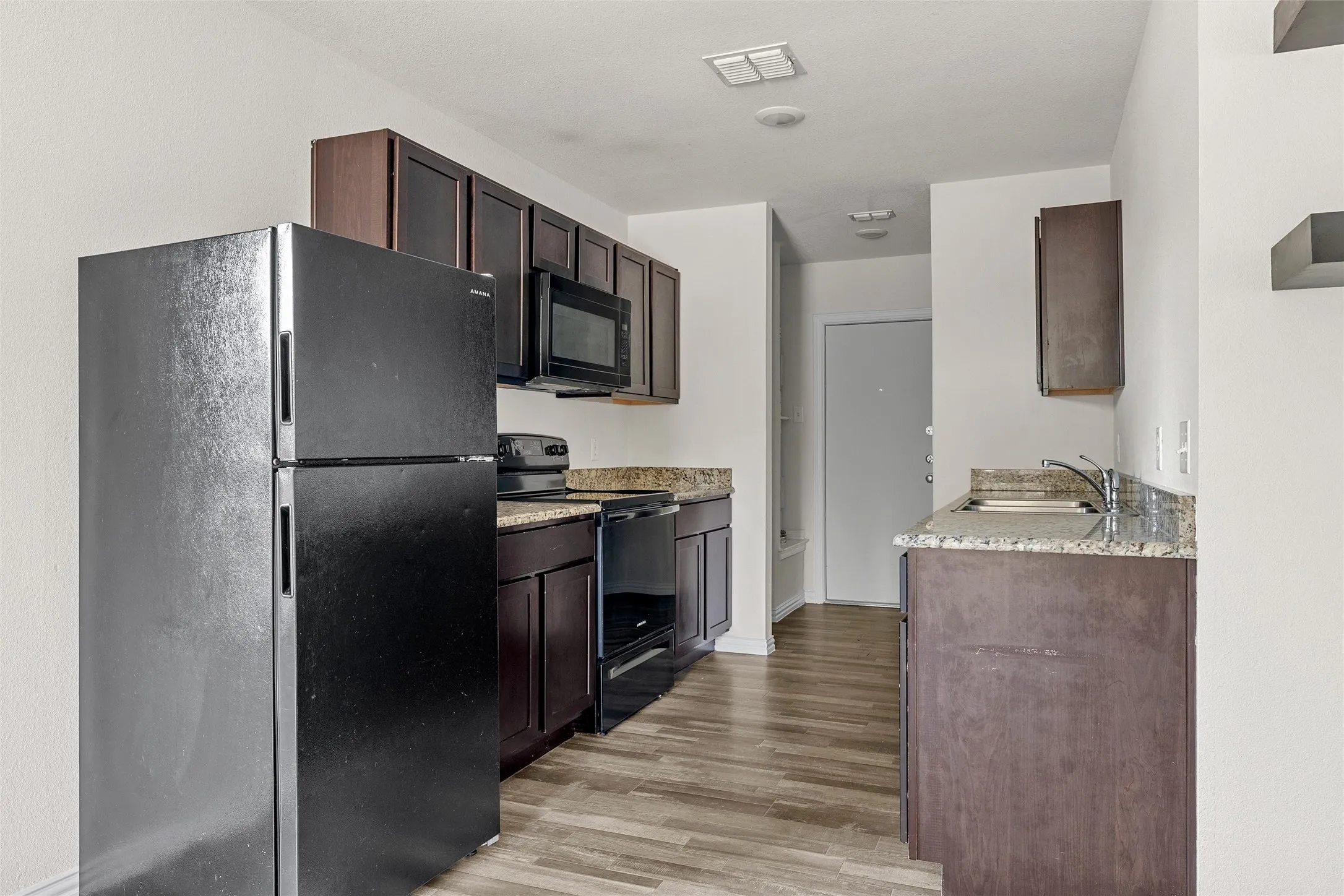 Kitchen featuring wood-finish flooring, dark wood cabinetry, and stone countertops