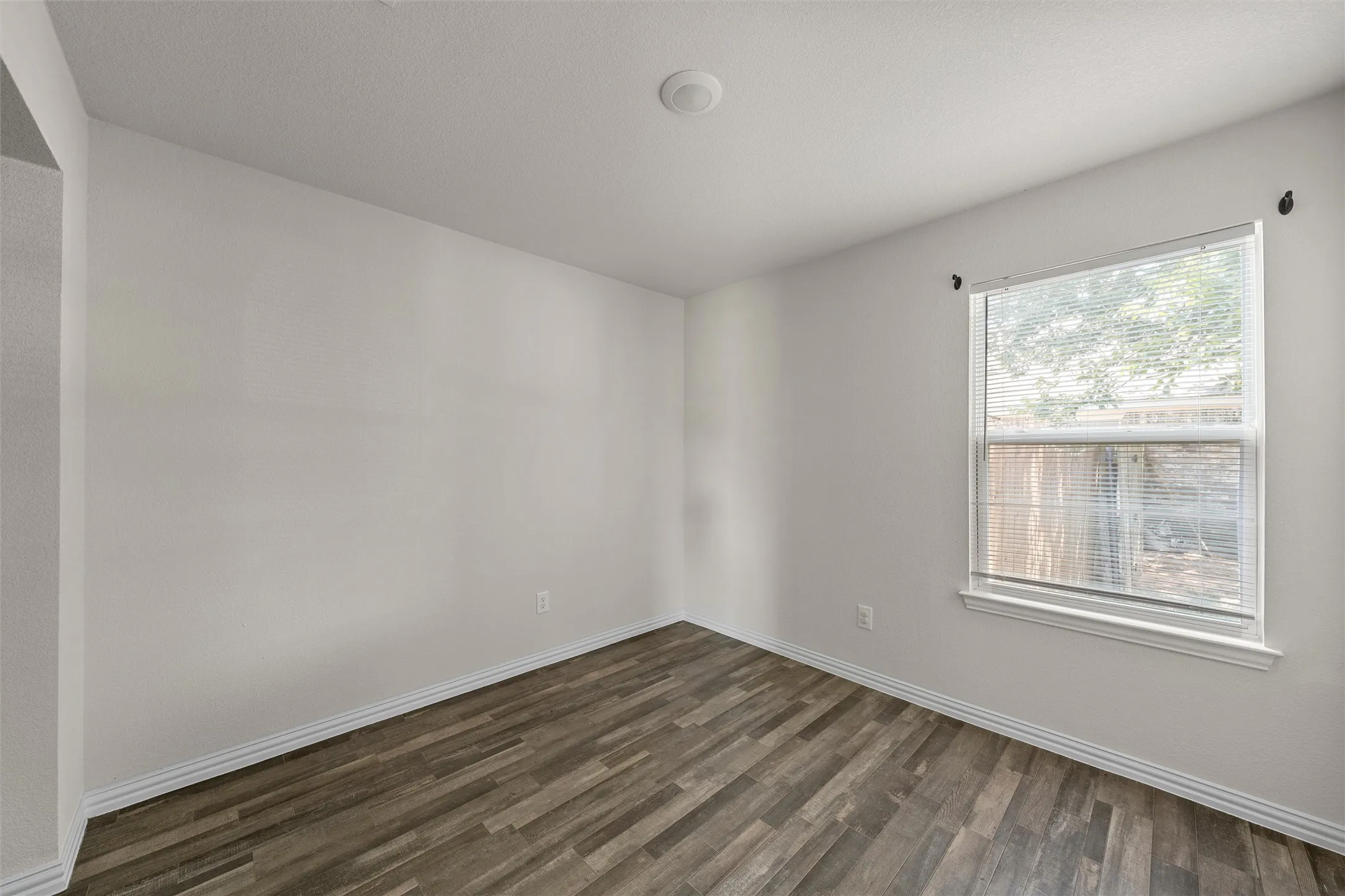 Wood-finish flooring, white walls, and a window with blinds