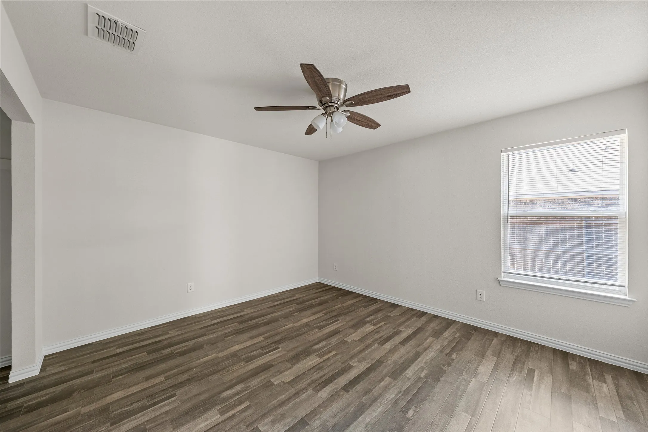 Wood-finish flooring, ceiling fan with integrated lighting, window with blinds, and light-toned walls