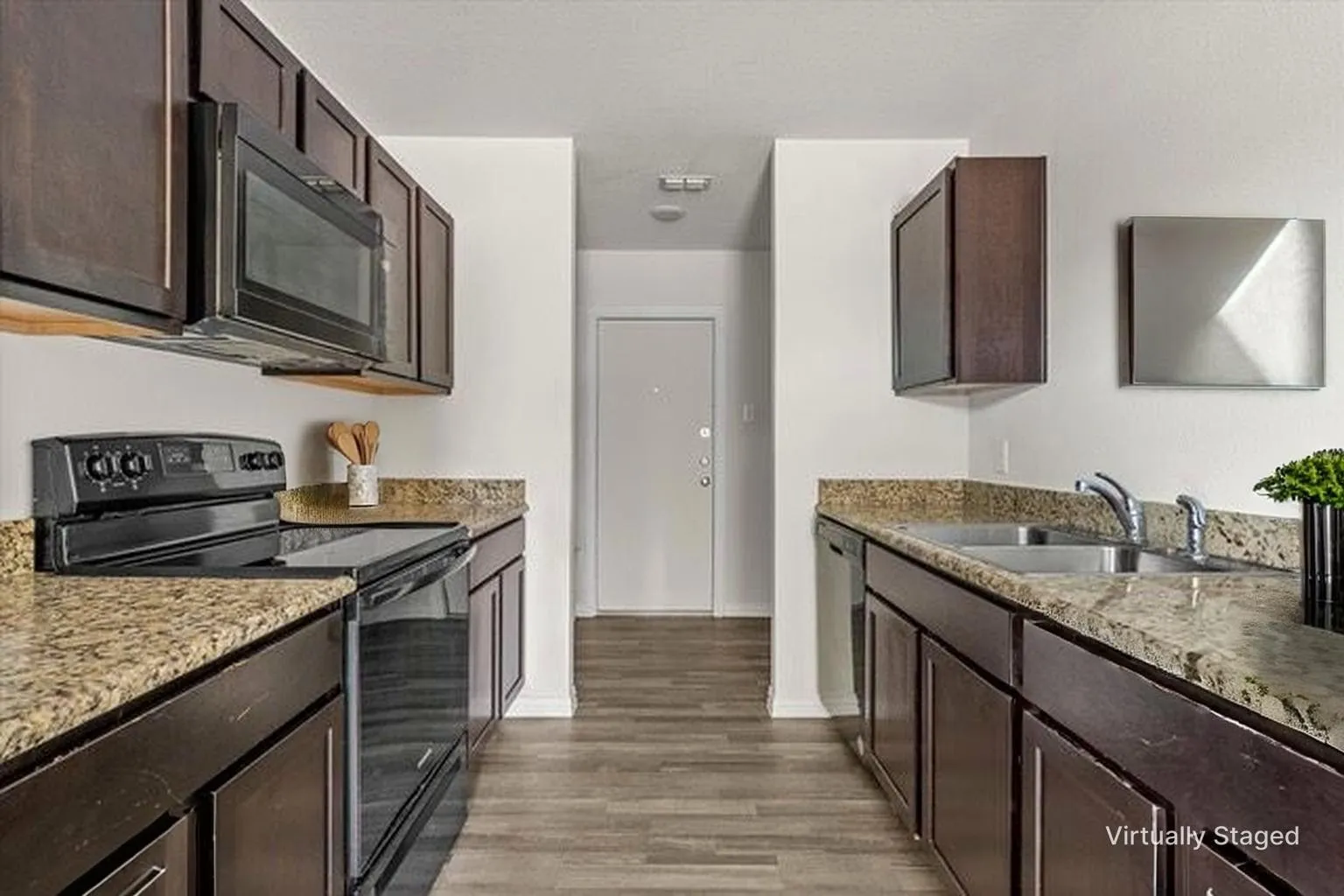 Galley kitchen with wood-finish flooring, dark wood cabinetry, and granite-style countertops