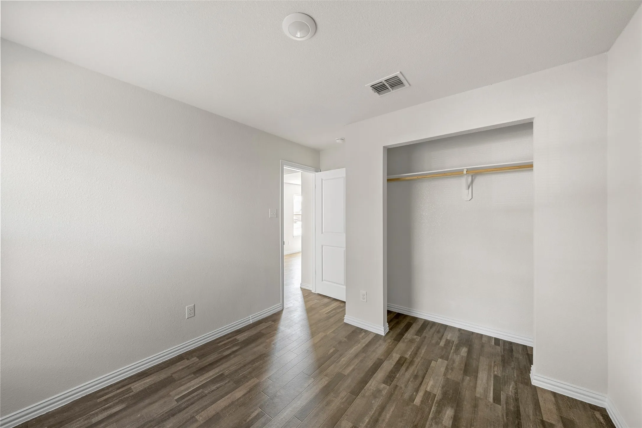 Spacious bedroom featuring wood-finish flooring, generous closet with rod and shelving, and abundant natural light from entry door