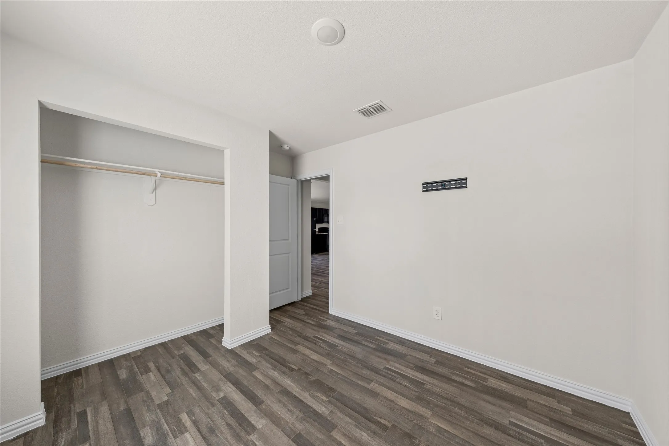 Wood-finish flooring, recessed ceiling light, white baseboards, and a built-in closet with hanging rod