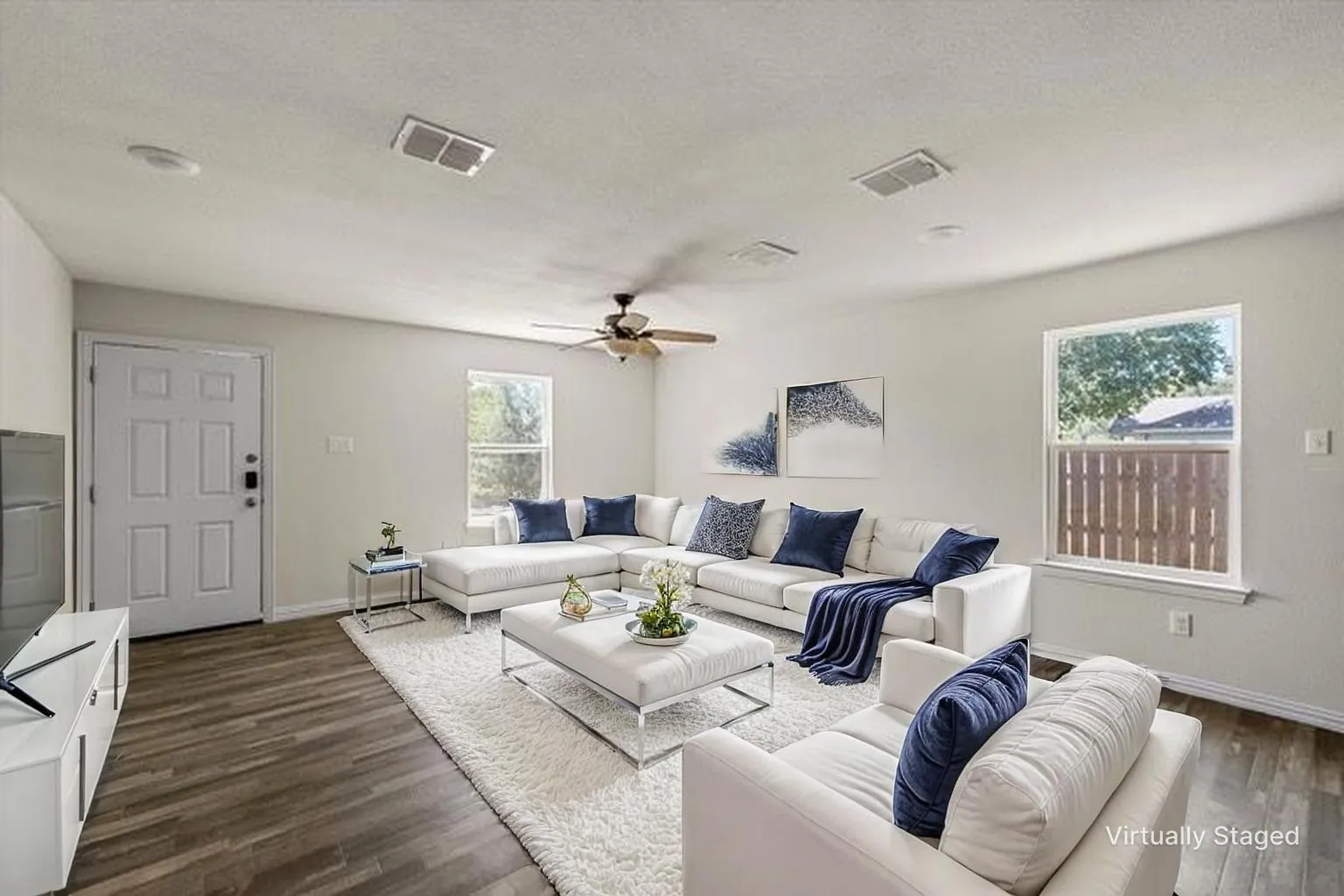 Spacious living area featuring wood-finish flooring, light-toned walls, multiple windows, and a ceiling fan