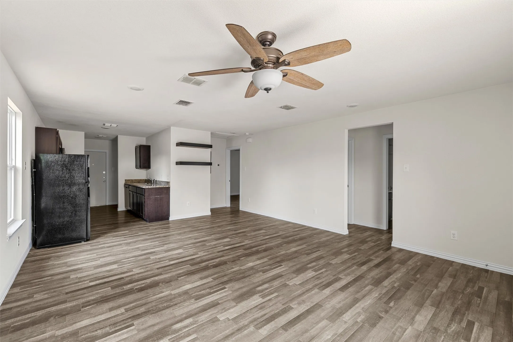 Expansive open-concept room featuring wood-finish flooring, a ceiling fan with integrated lighting, and white walls