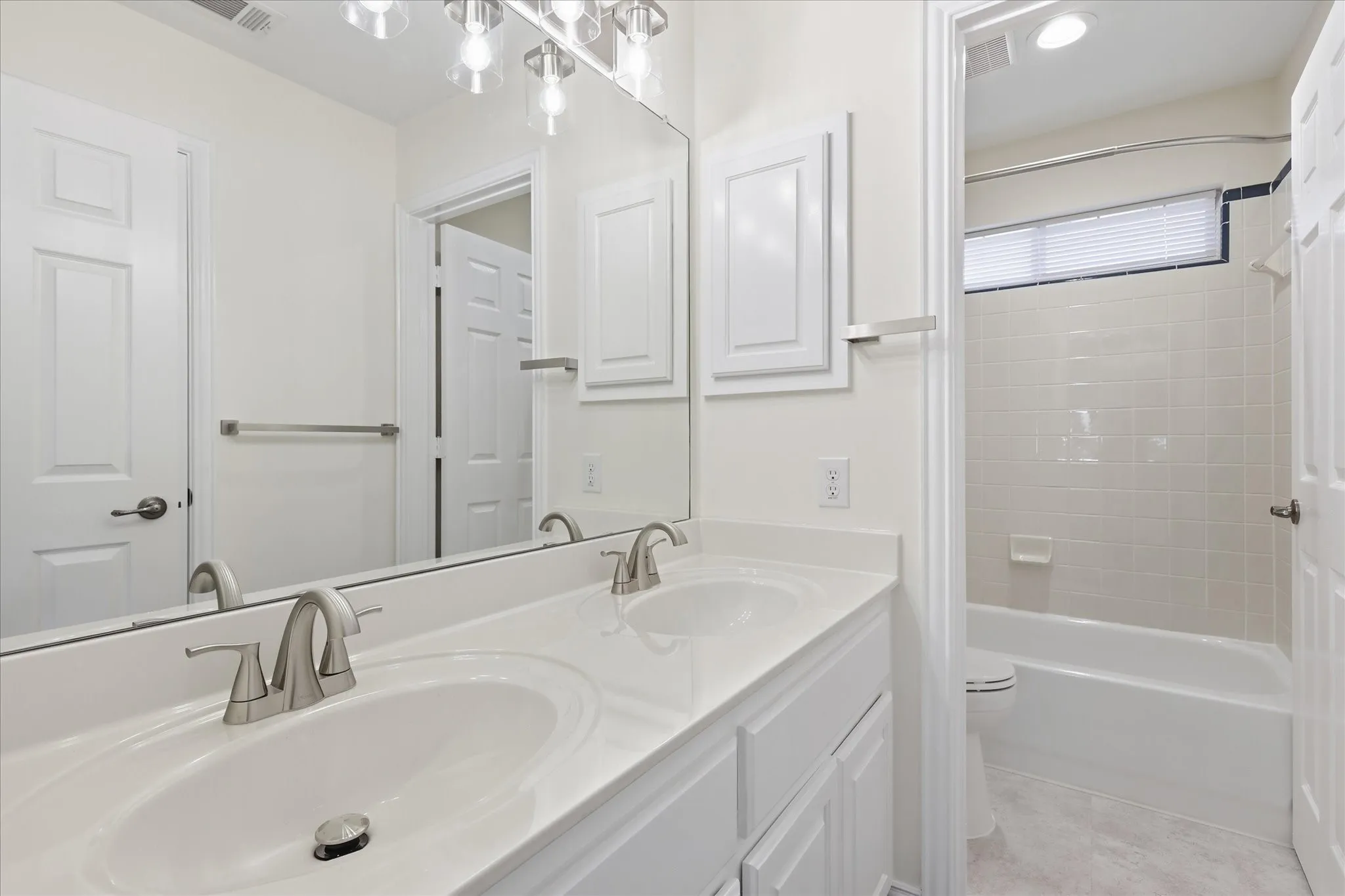Double vanity with integrated sinks, brushed nickel fixtures, a full-width mirror, and overhead lighting