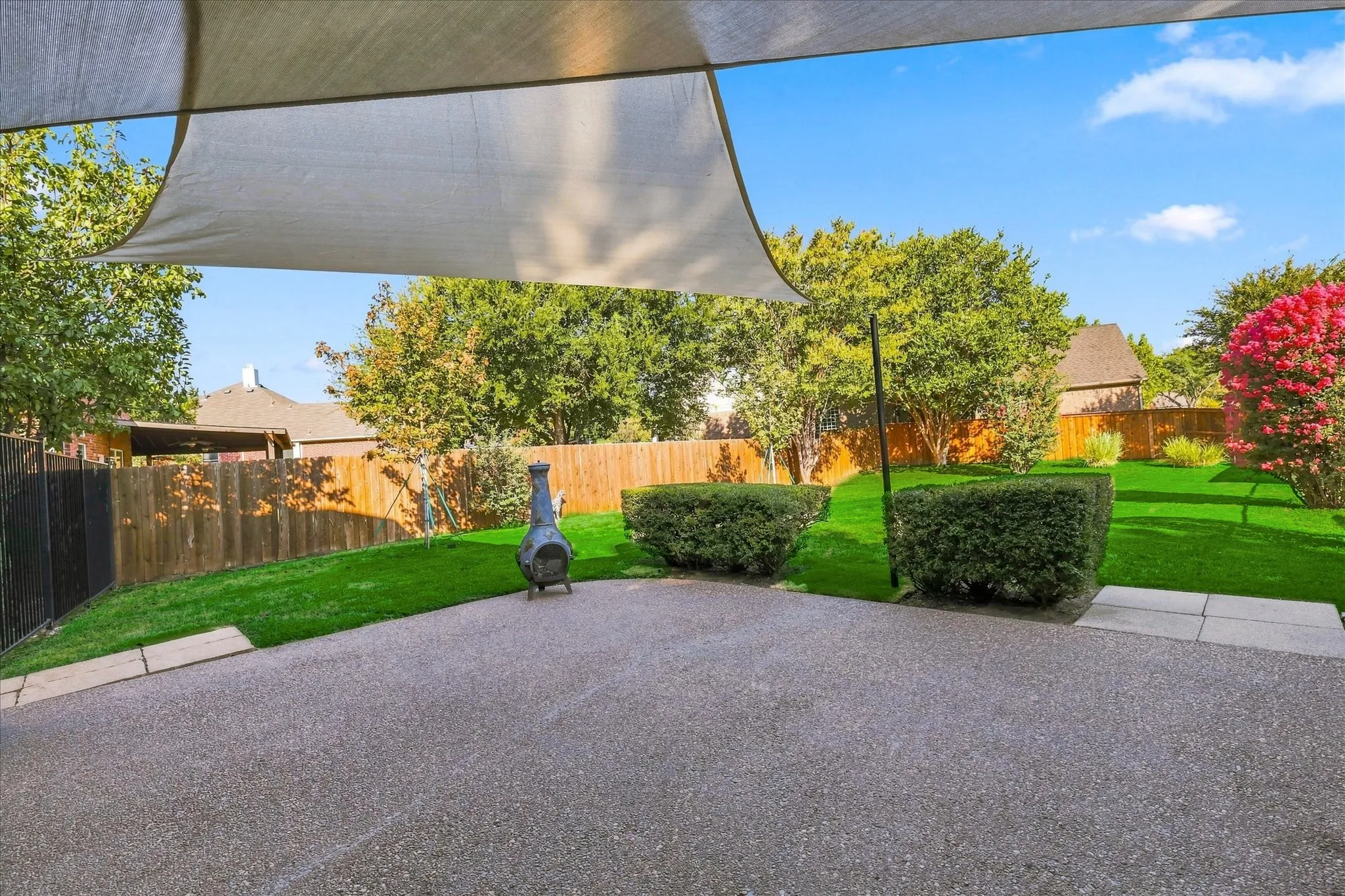 Expansive outdoor patio with shade sail, textured concrete surface, artificial turf, and wood privacy fencing