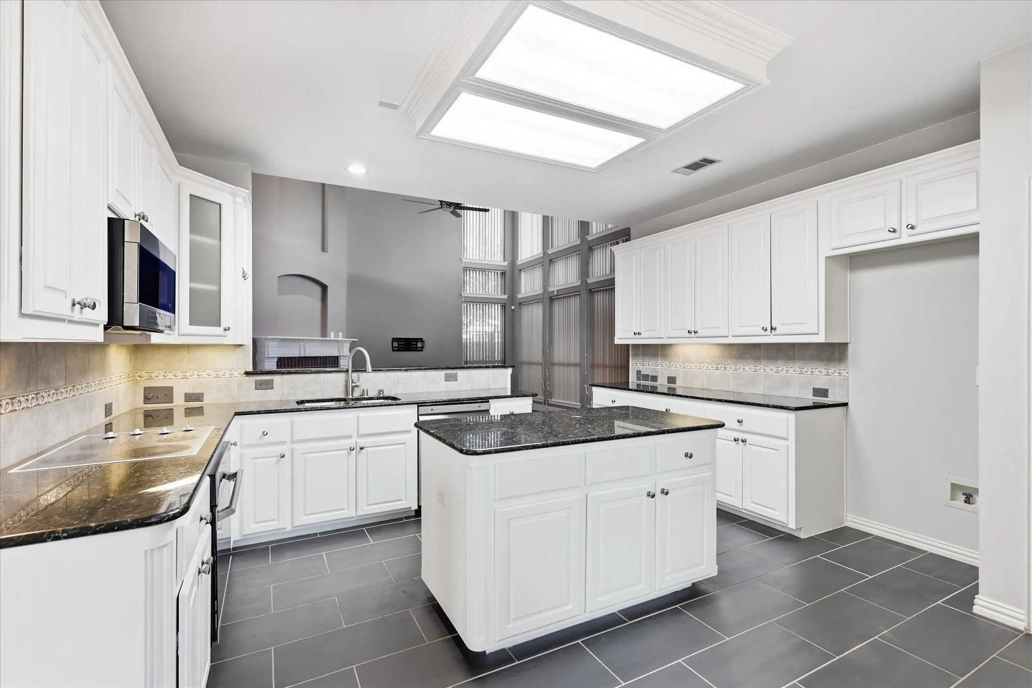 Kitchen featuring dark stone countertops, white cabinetry, a built-in microwave, a central island, and tiled flooring