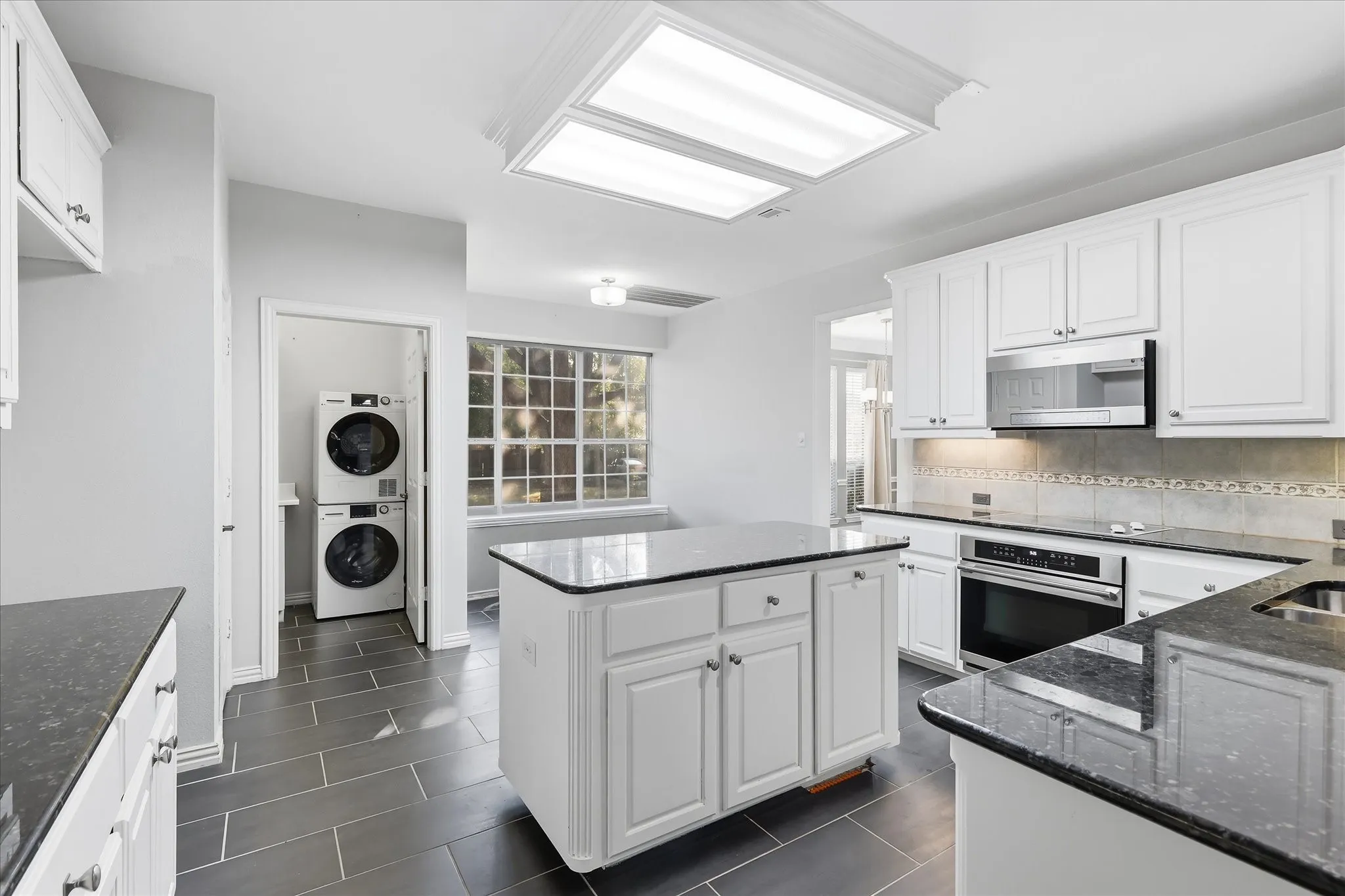 Kitchen featuring white cabinetry, dark stone countertops, stainless steel appliances, a center island with storage, and tiled flooring