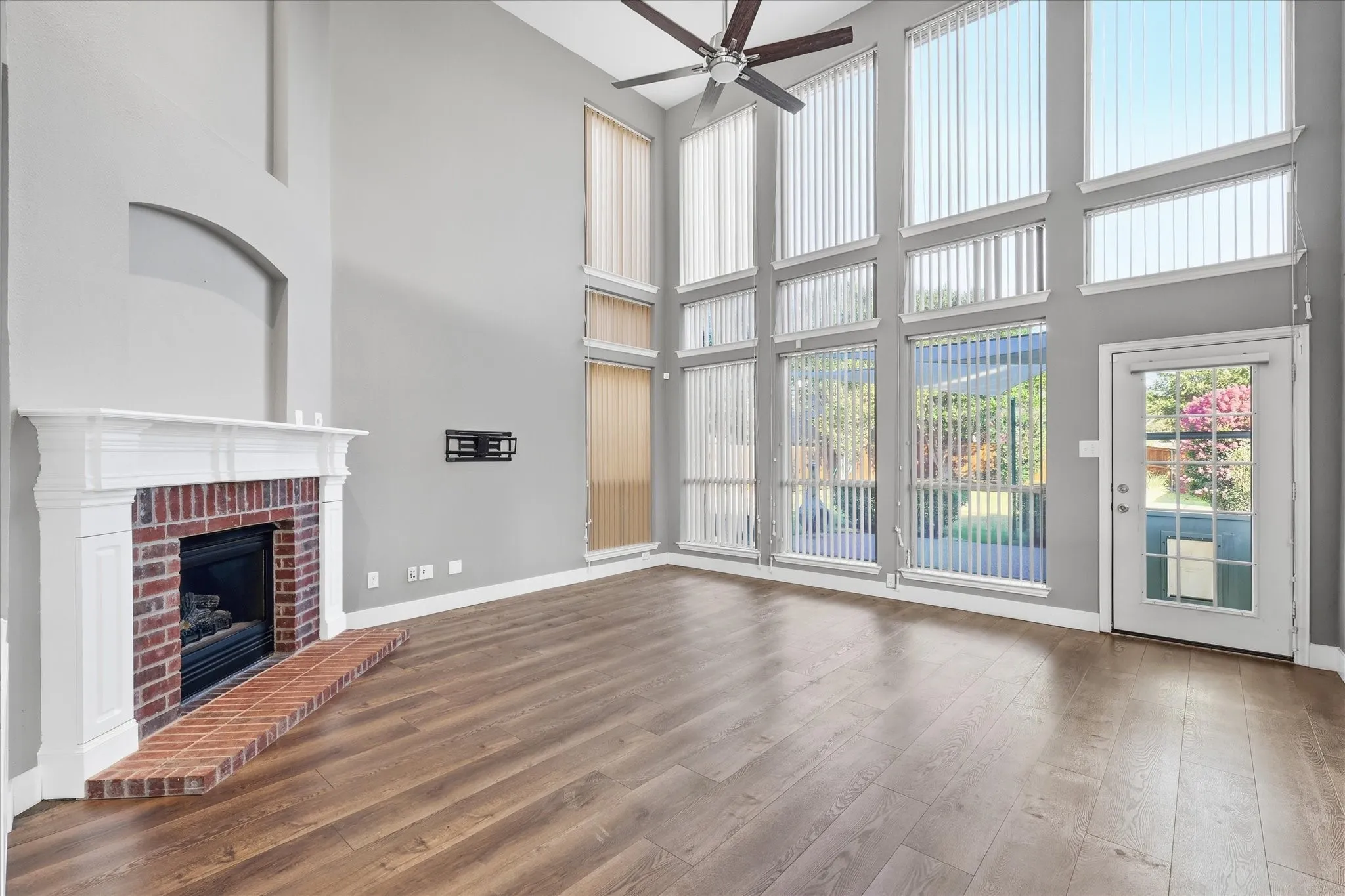 Two-story living area with wood-finish flooring, a brick fireplace with a white mantel, and a ceiling fan