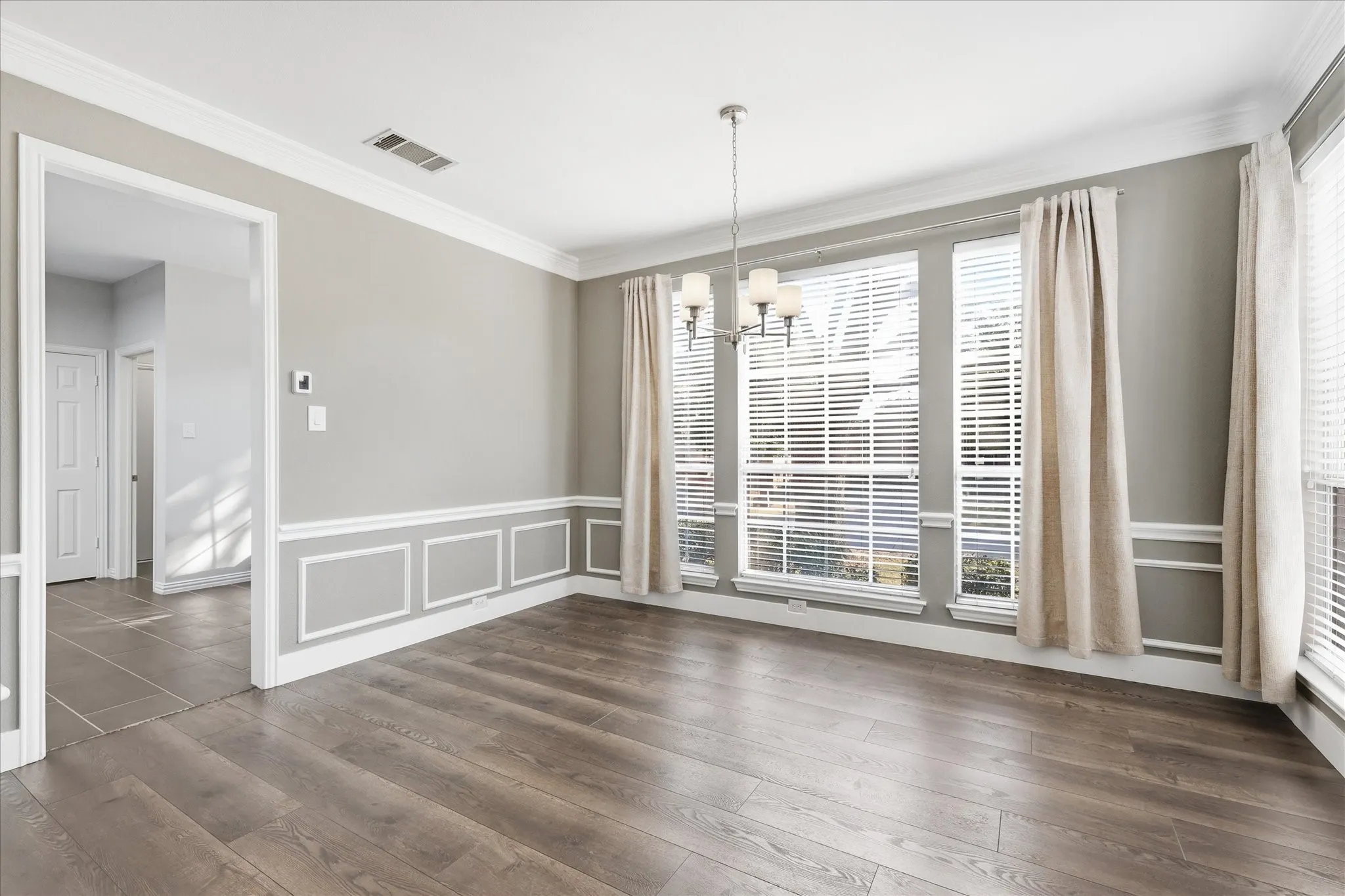 Wood-finish flooring, wainscoting with decorative trim, multiple large windows, and a chandelier lighting fixture