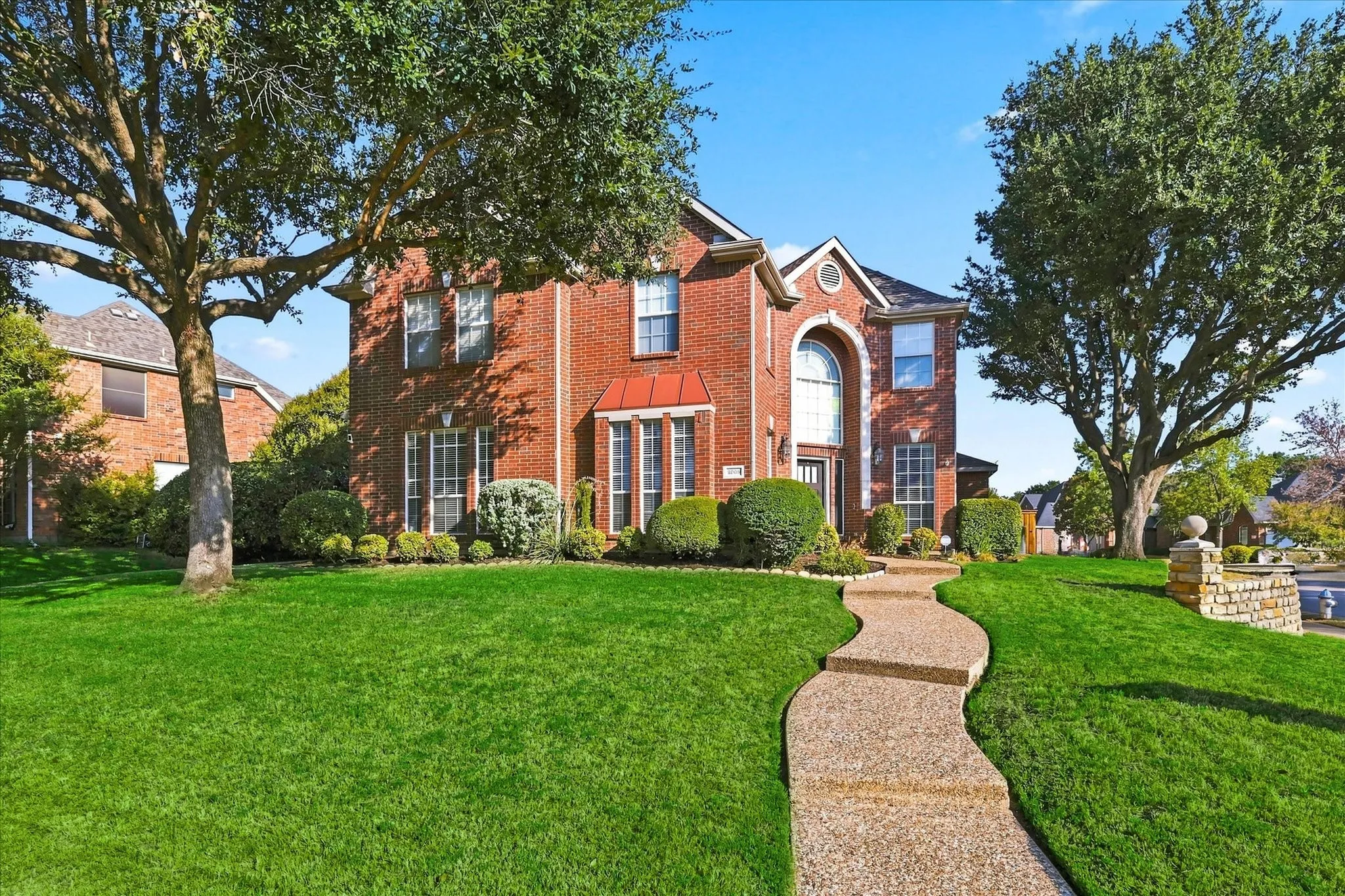 Red brick exterior with arched entry, bay window with metal roof, and stone pathway