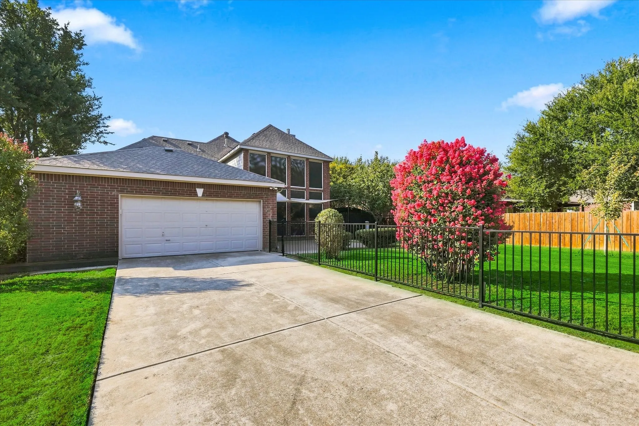Brick exterior, attached garage, concrete driveway, iron fencing, and established landscaping