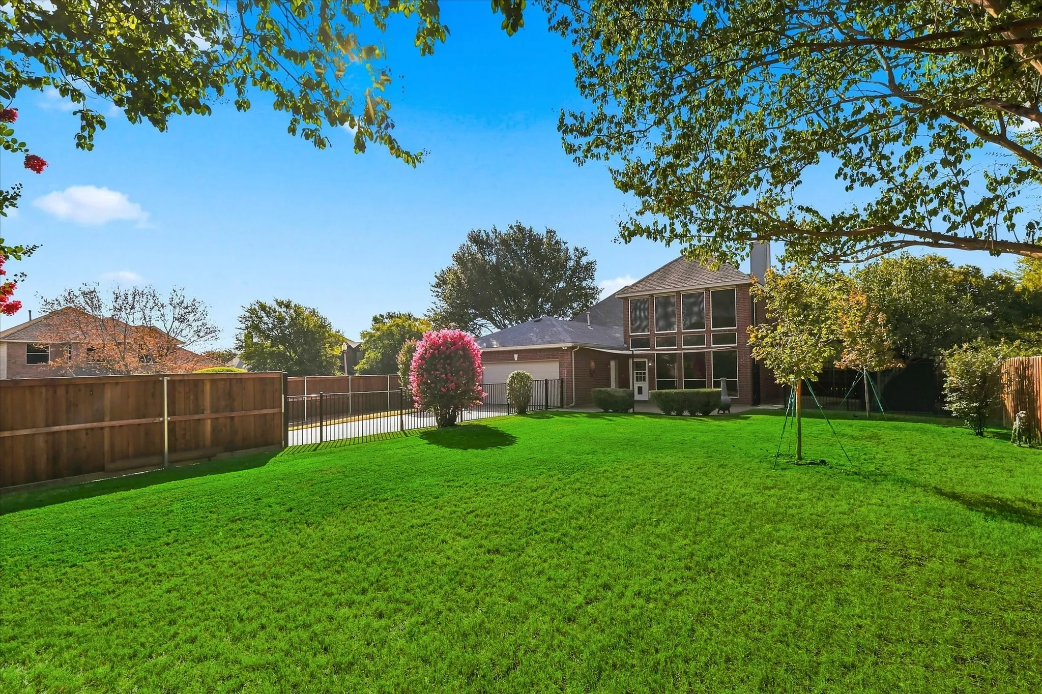 Expansive green lawn featuring mature trees, a privacy fence, and a brick exterior with multiple windows