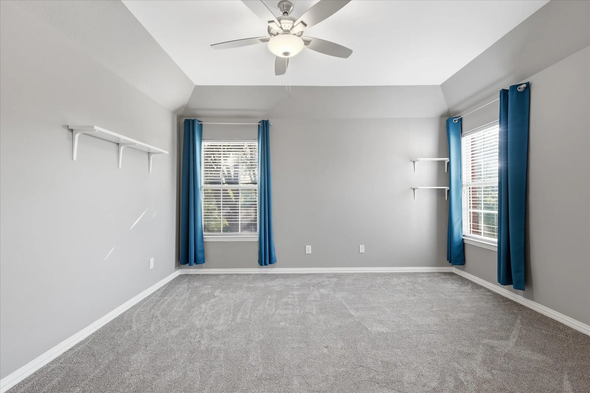 Vaulted ceiling with a ceiling fan, dual windows, wall-mounted shelving, and carpeted flooring