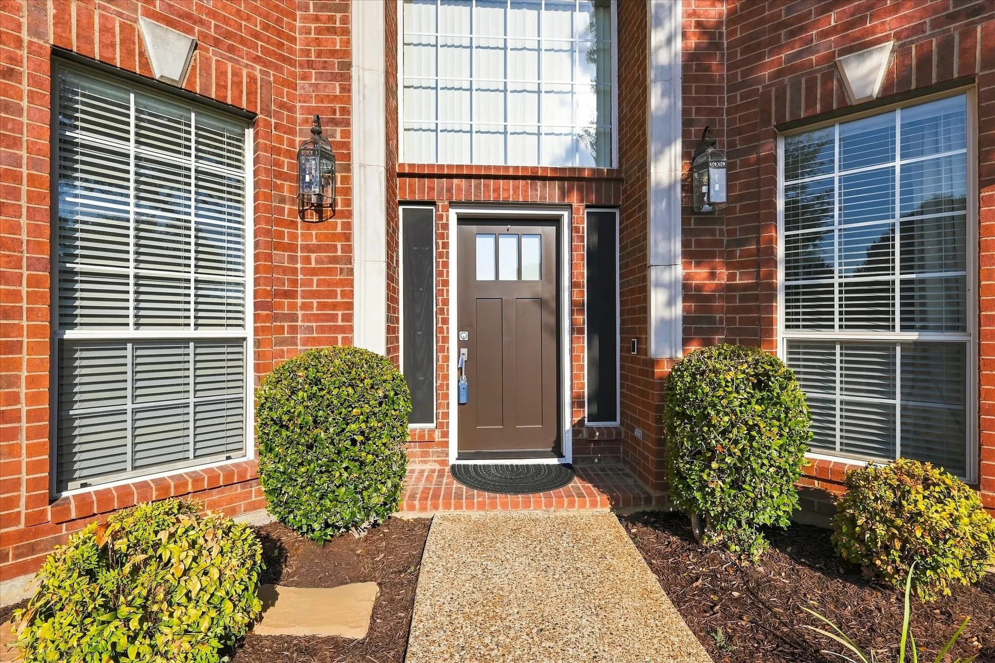Brick facade featuring a brown paneled entry door, transom window, and dual outdoor lanterns
