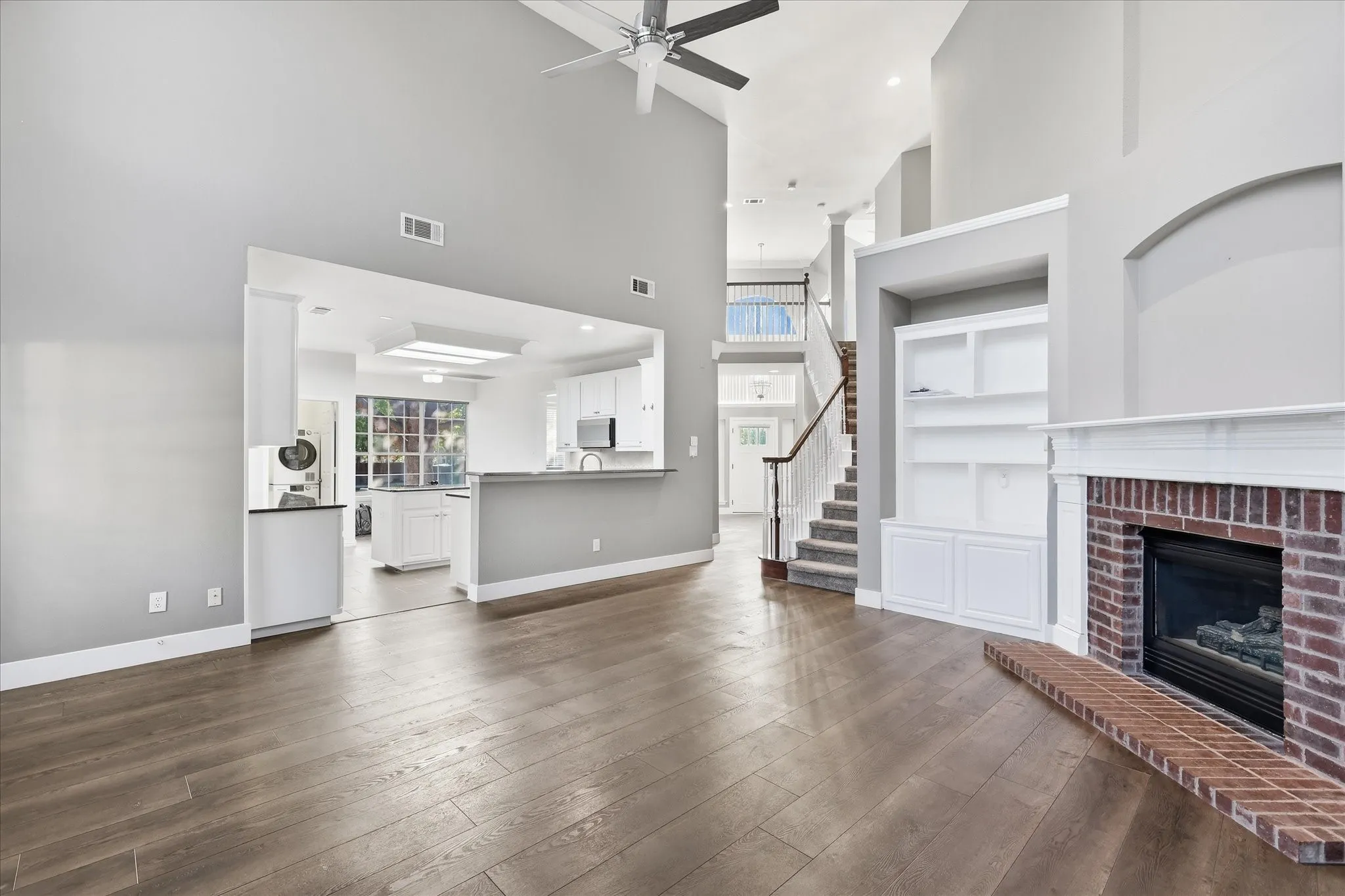Vaulted ceilings, wood-finish flooring, brick fireplace, built-in cabinetry, and a ceiling fan