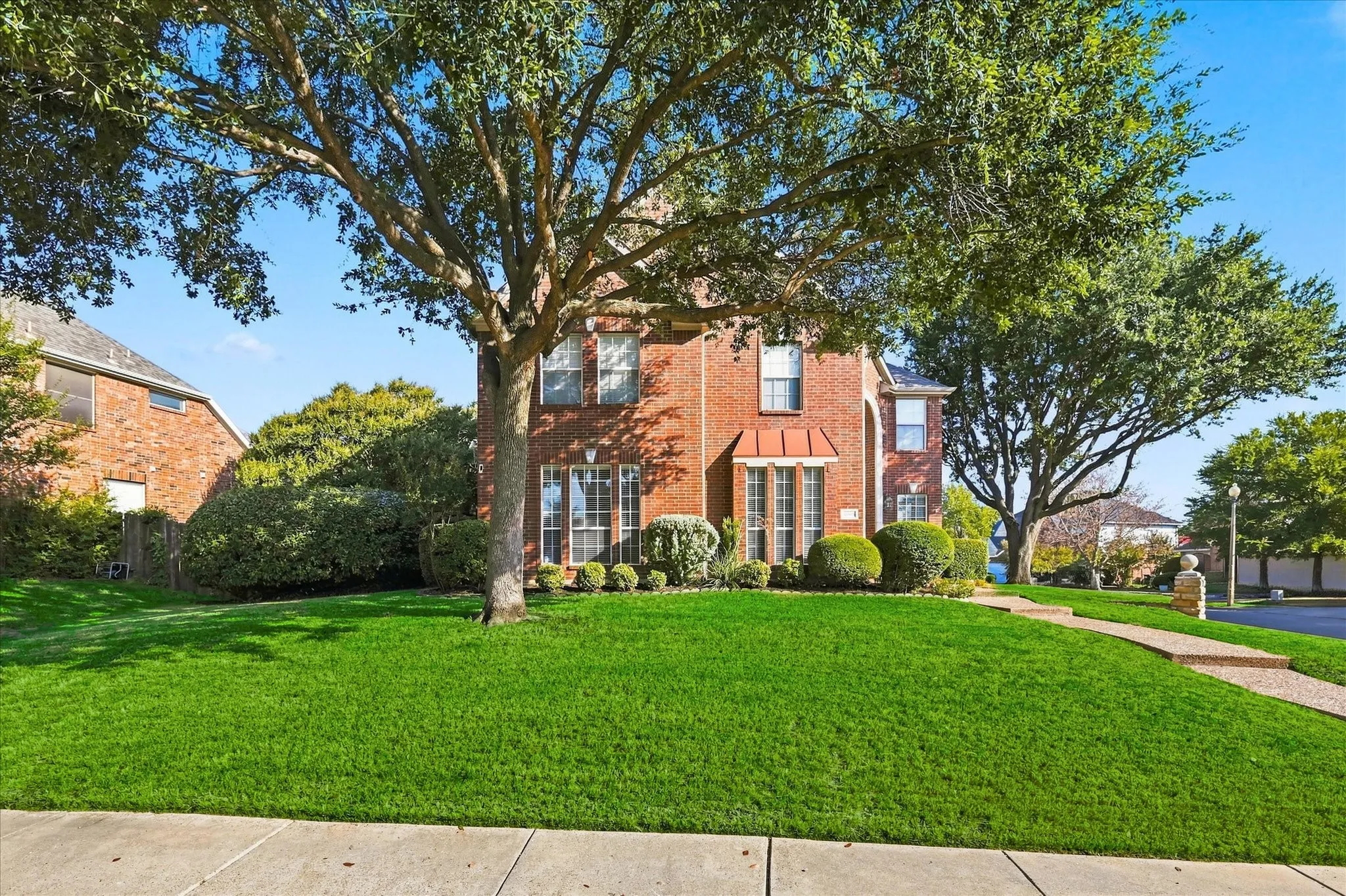 Brick exterior with mature trees, a manicured lawn, and a stone-paver walkway