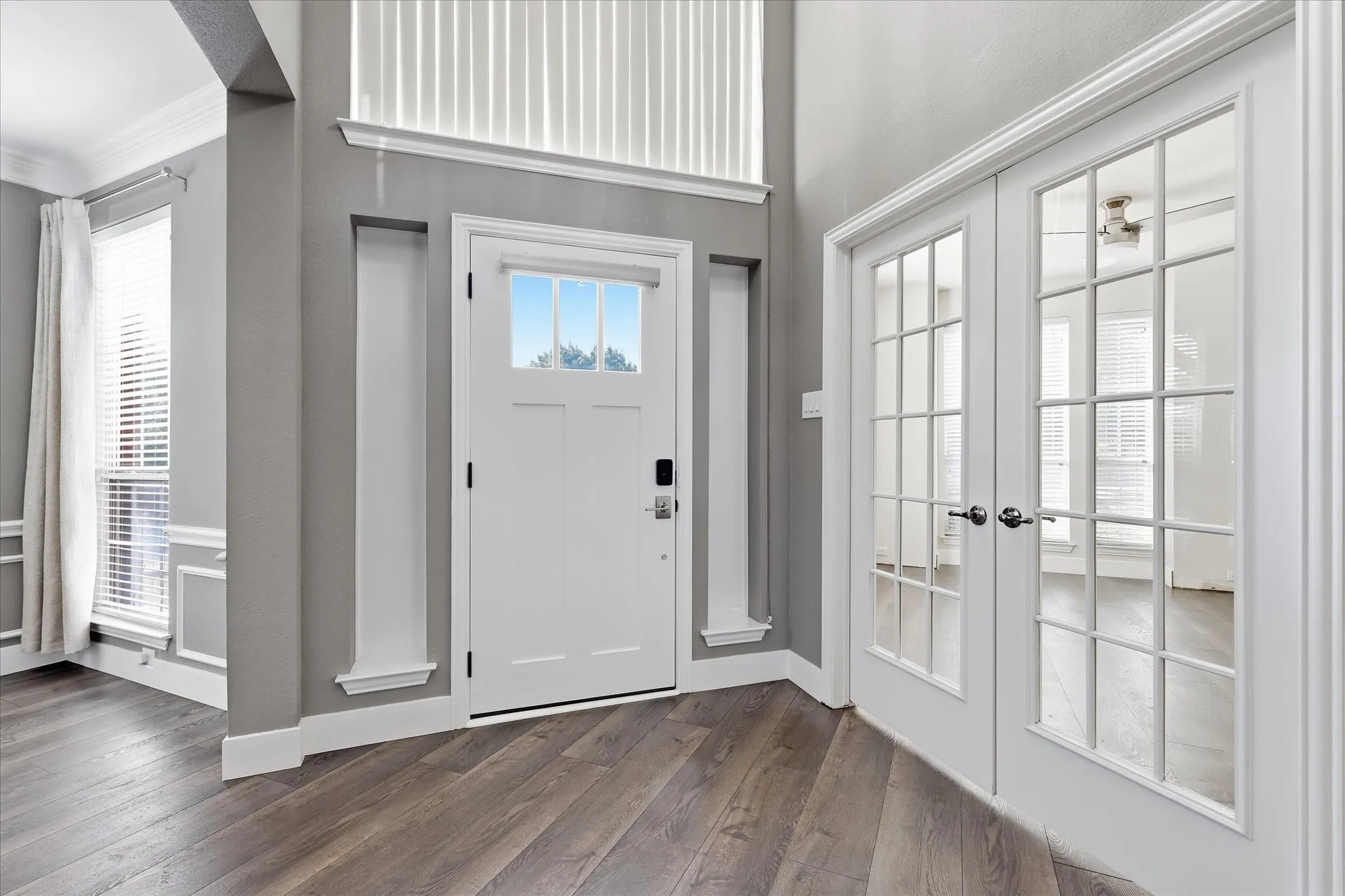 Entryway featuring wood-finish flooring, a white paneled entry door with transom window, and adjacent French doors