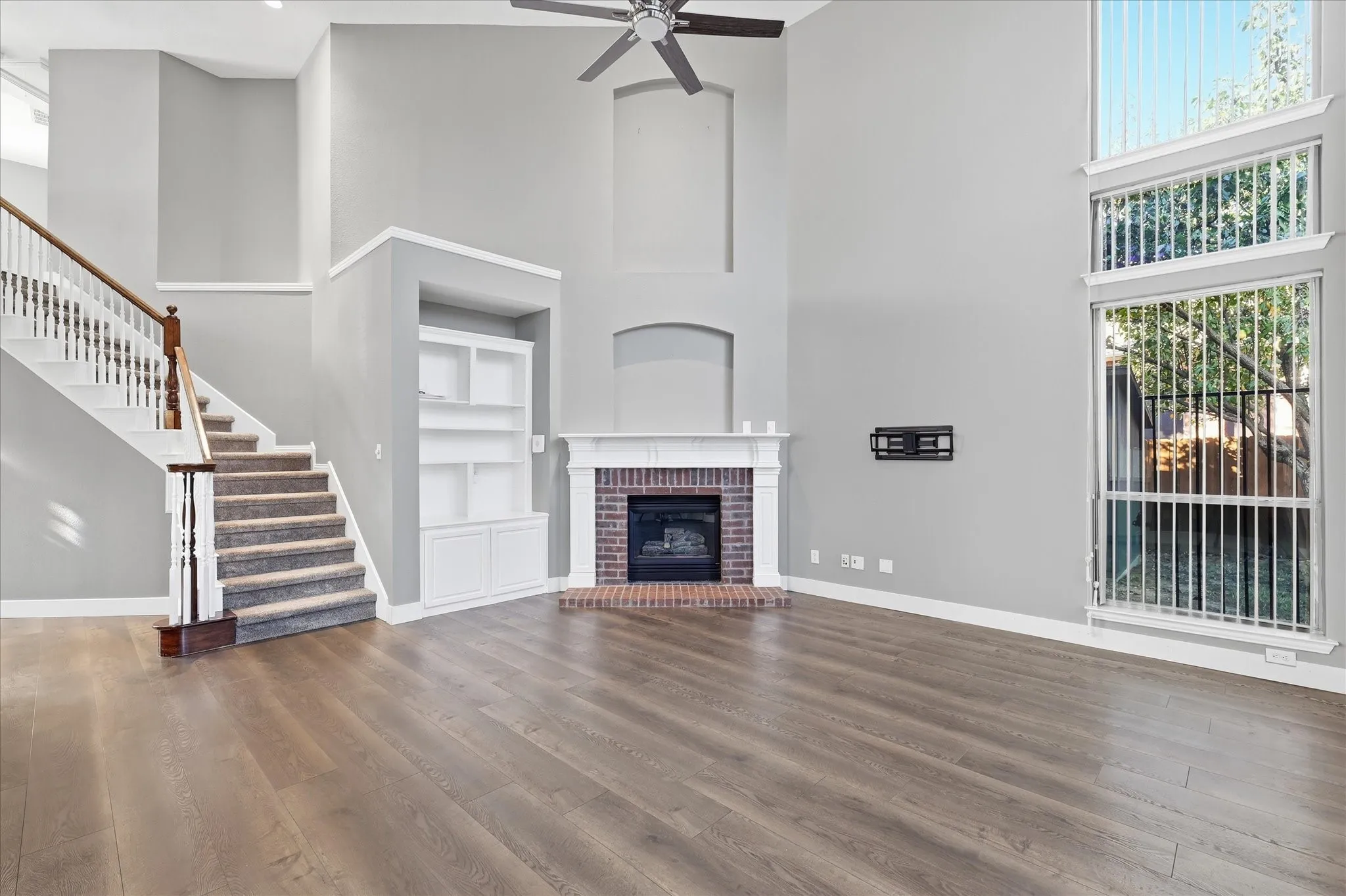 Spacious living area featuring wood-finish flooring, a brick fireplace with a white mantel, and built-in shelving