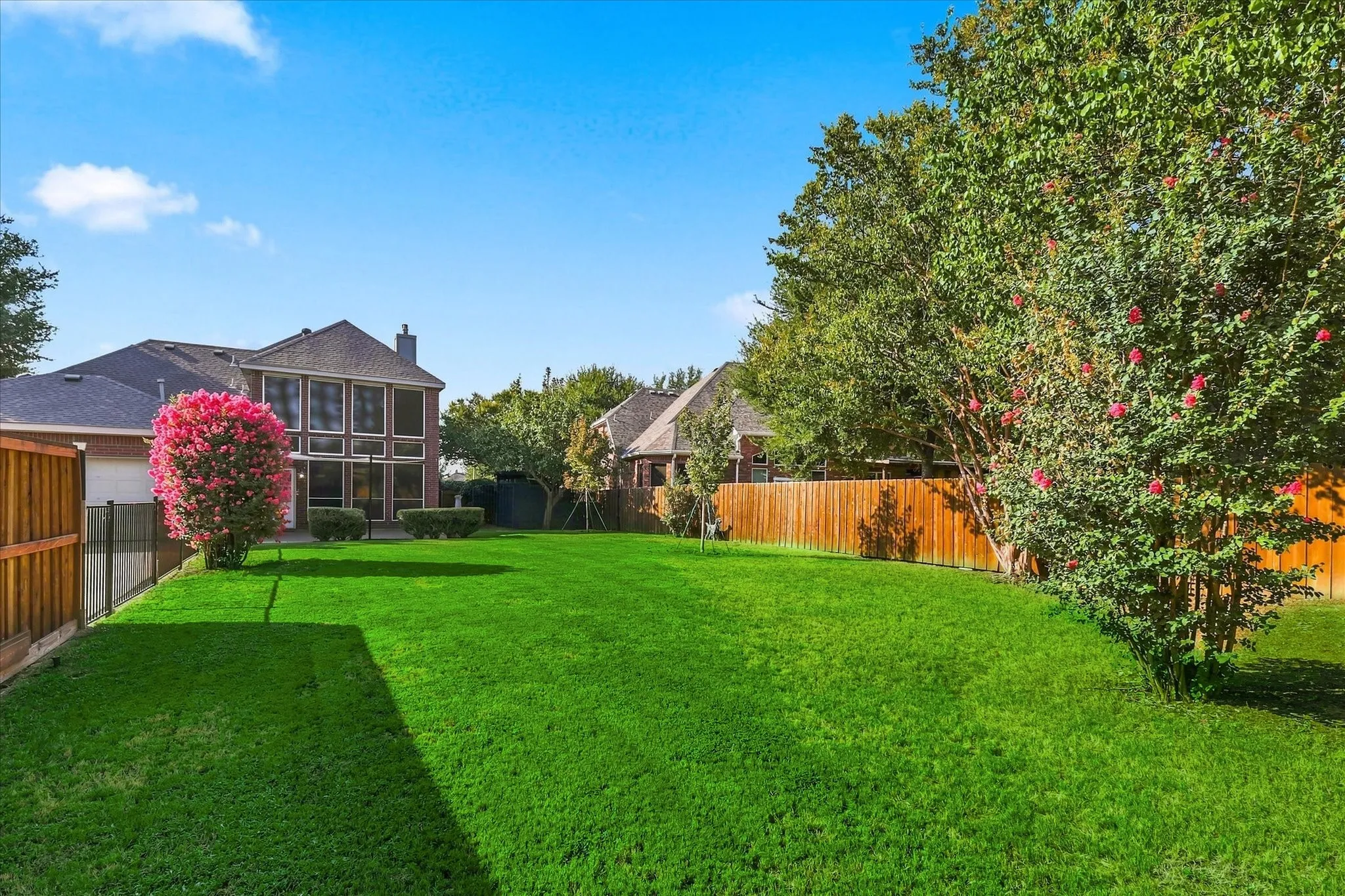 Expansive backyard with a manicured lawn, wood fencing, and mature trees