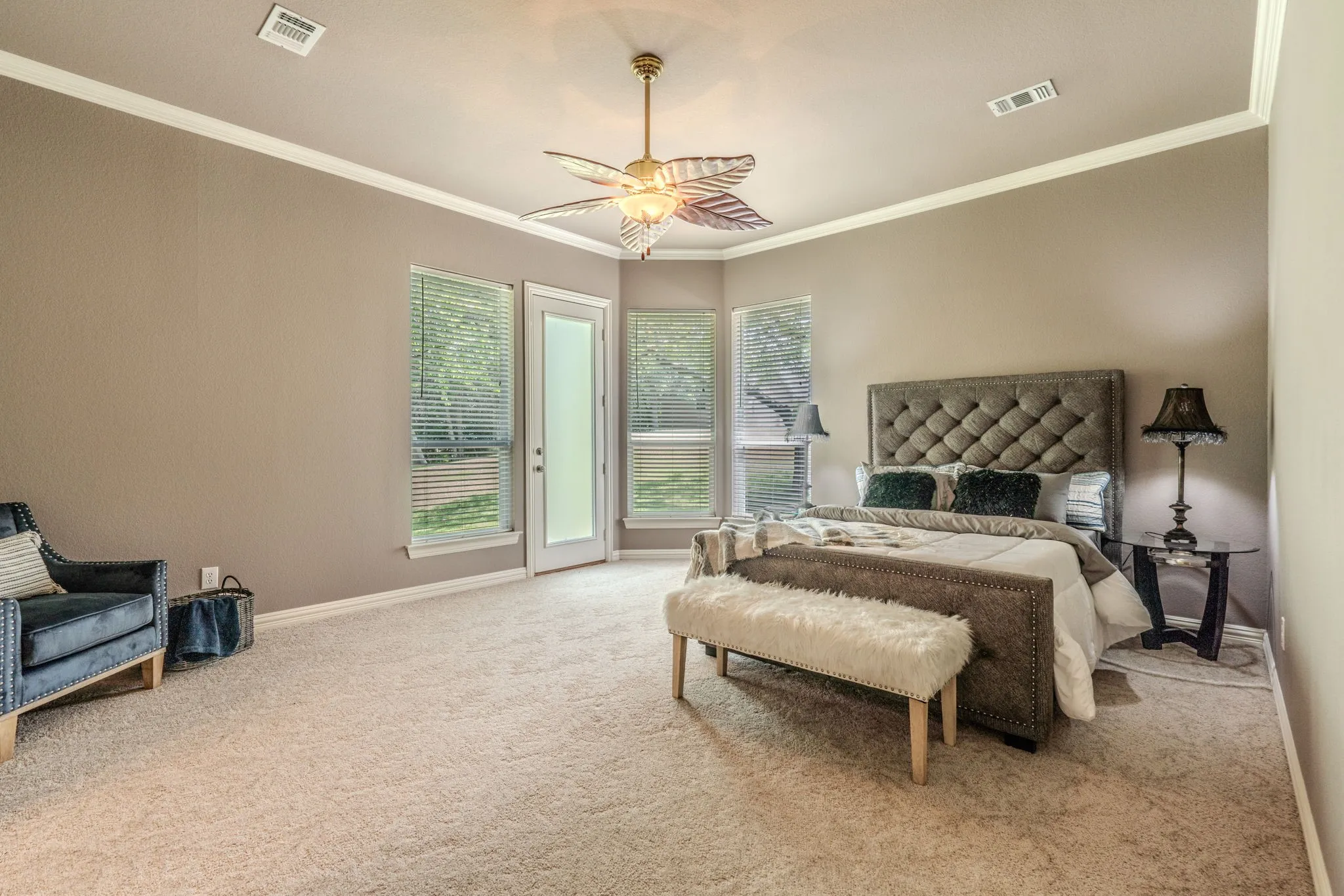 Huge primary bedroom with space for a sitting area, crown molding, natural light and an exterior door leading out onto a patio.