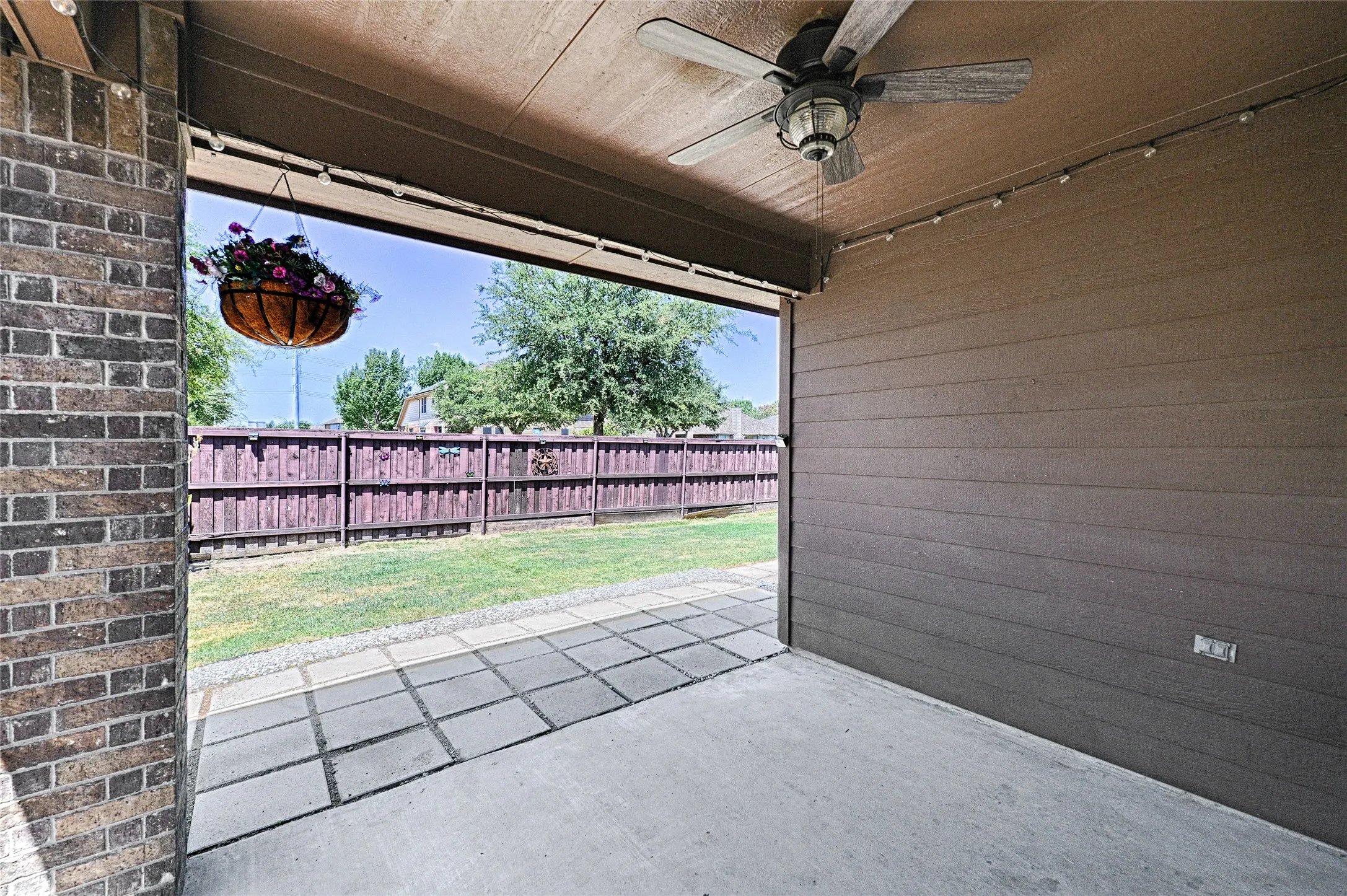 Covered patio featuring a ceiling fan, string lighting, concrete flooring, and brick wall accents
