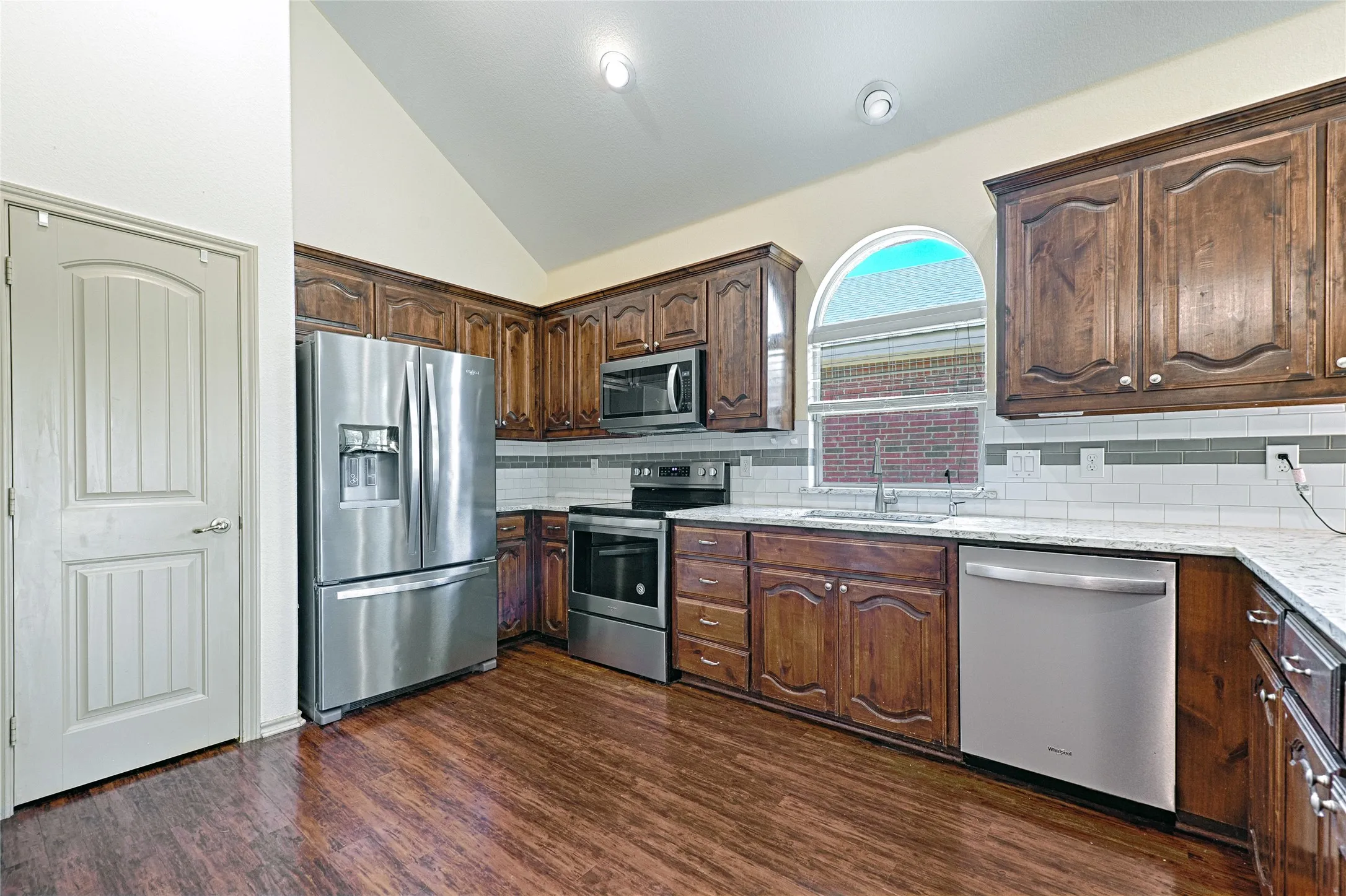 Kitchen featuring rich wood cabinetry, stainless steel appliances, a white subway tile backsplash, and wood-finish flooring
