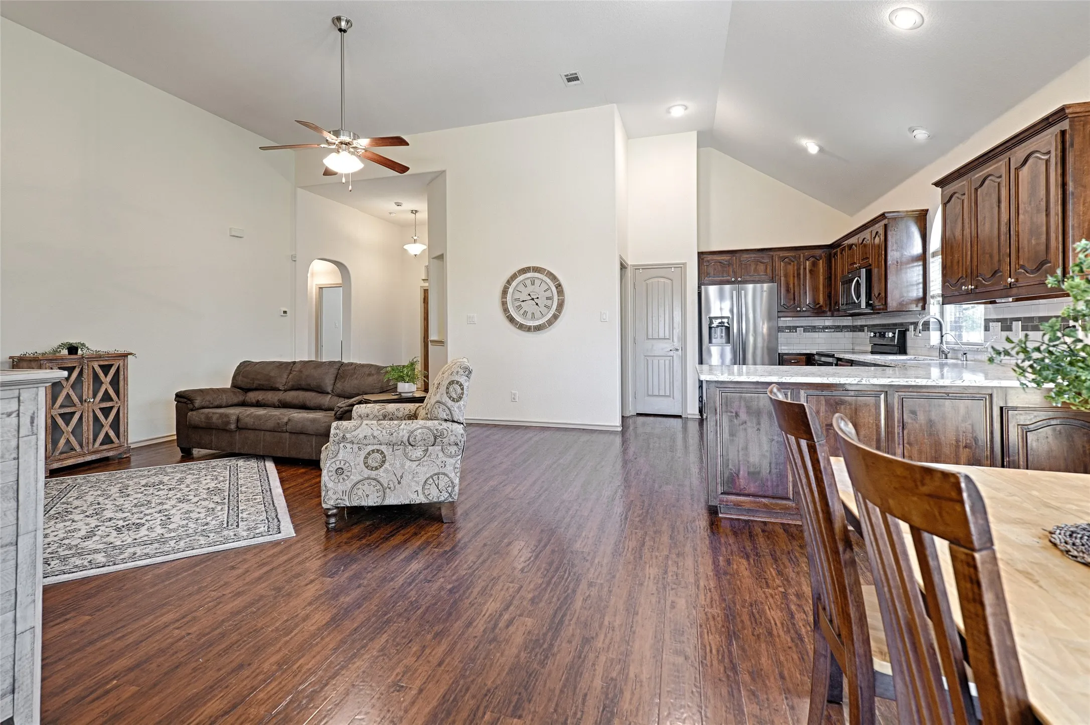 Open-concept living space featuring vaulted ceilings, wood-finish flooring, a kitchen island with seating, dark wood cabinetry, and recessed lighting