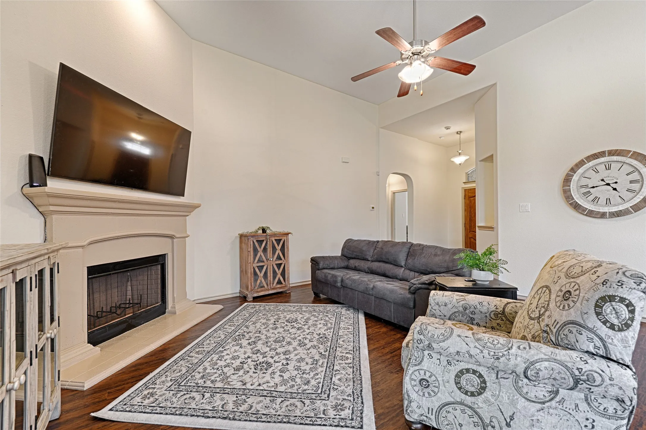 Living area featuring a fireplace with a stone-finish mantel, wood-finish flooring, and a ceiling fan with integrated lighting