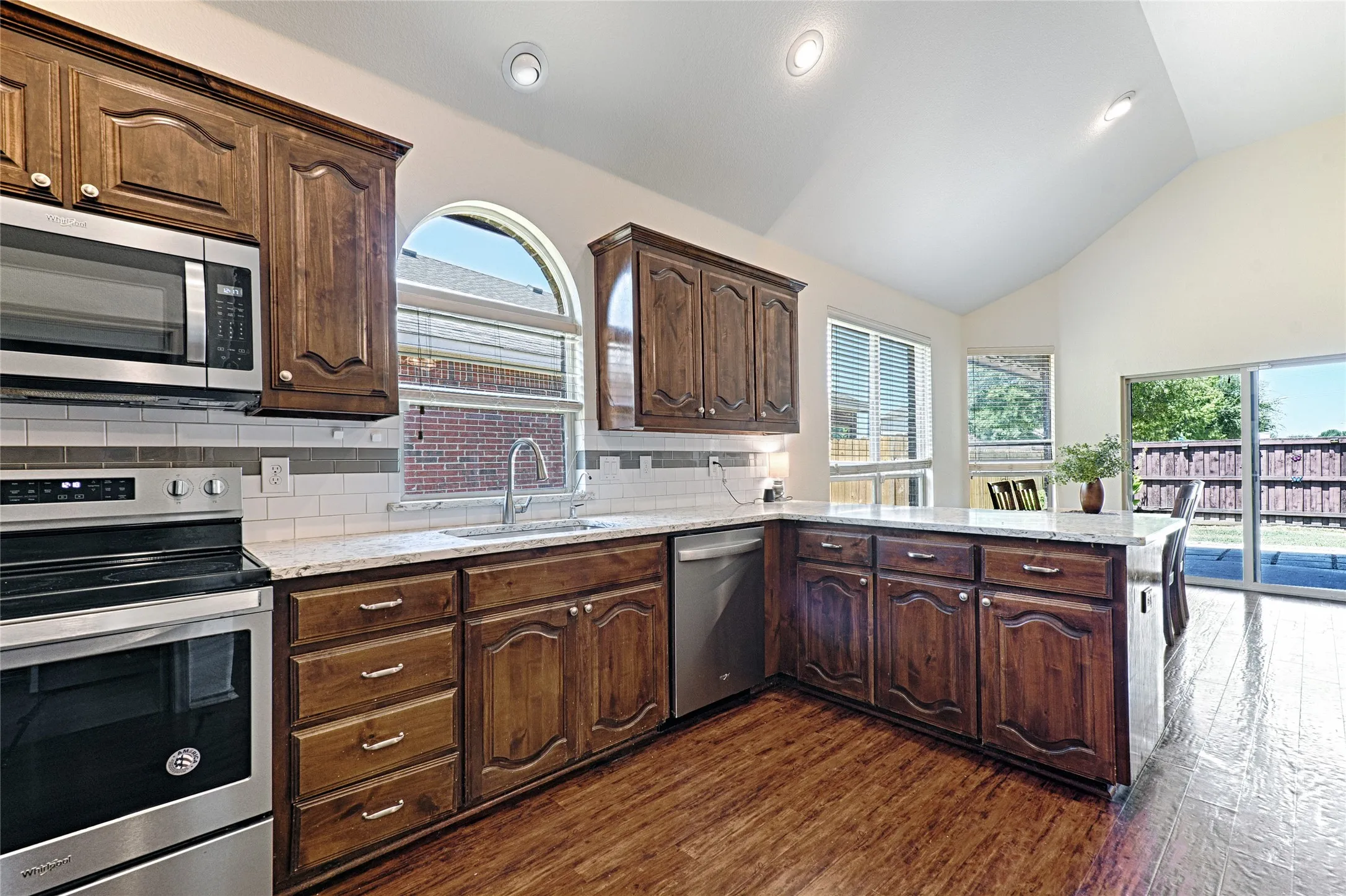 Kitchen featuring wood-finish flooring, stainless steel appliances, and a vaulted ceiling