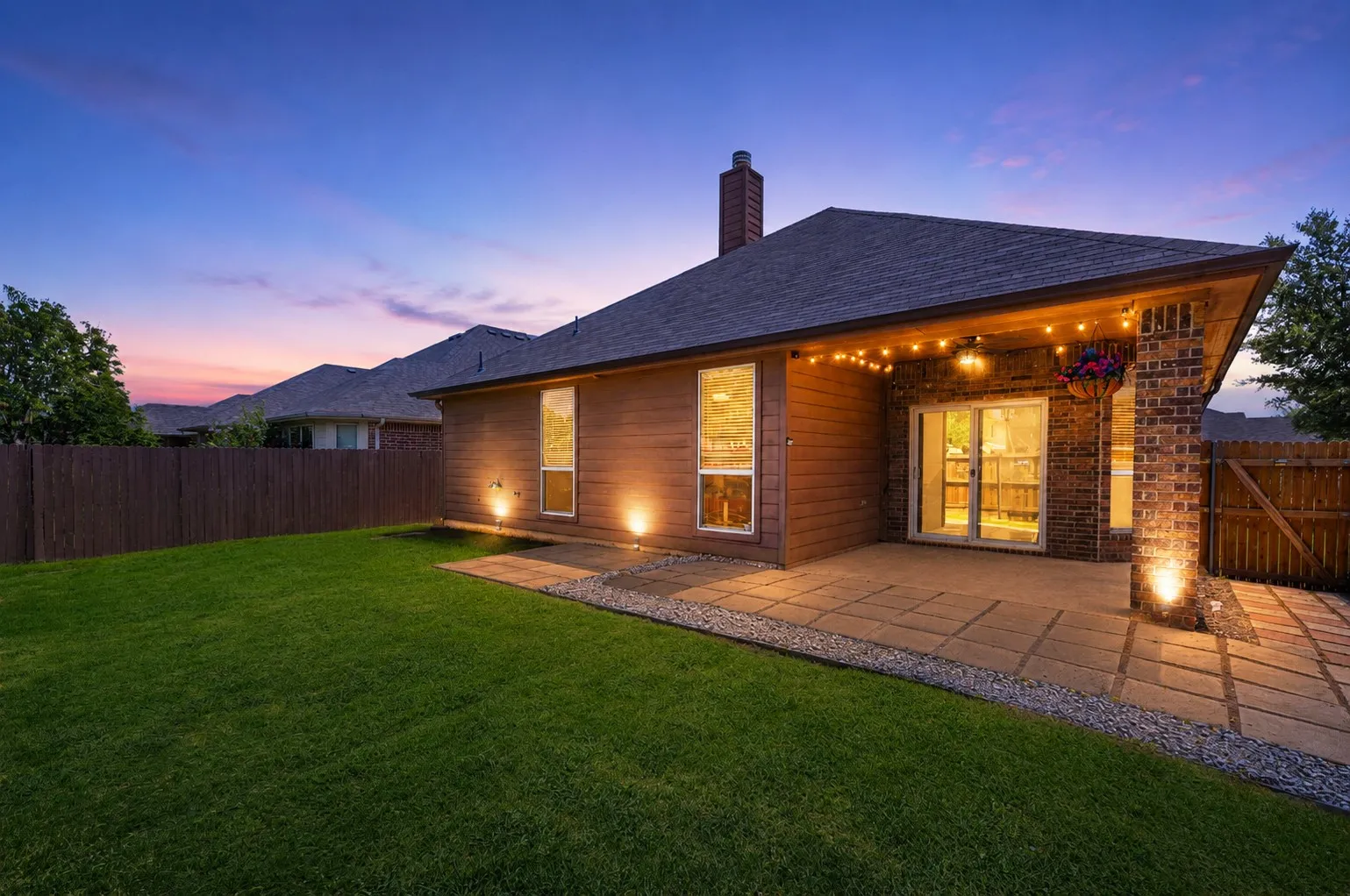 Expansive backyard featuring a manicured lawn, full privacy fencing, and a paver patio with integrated landscape lighting