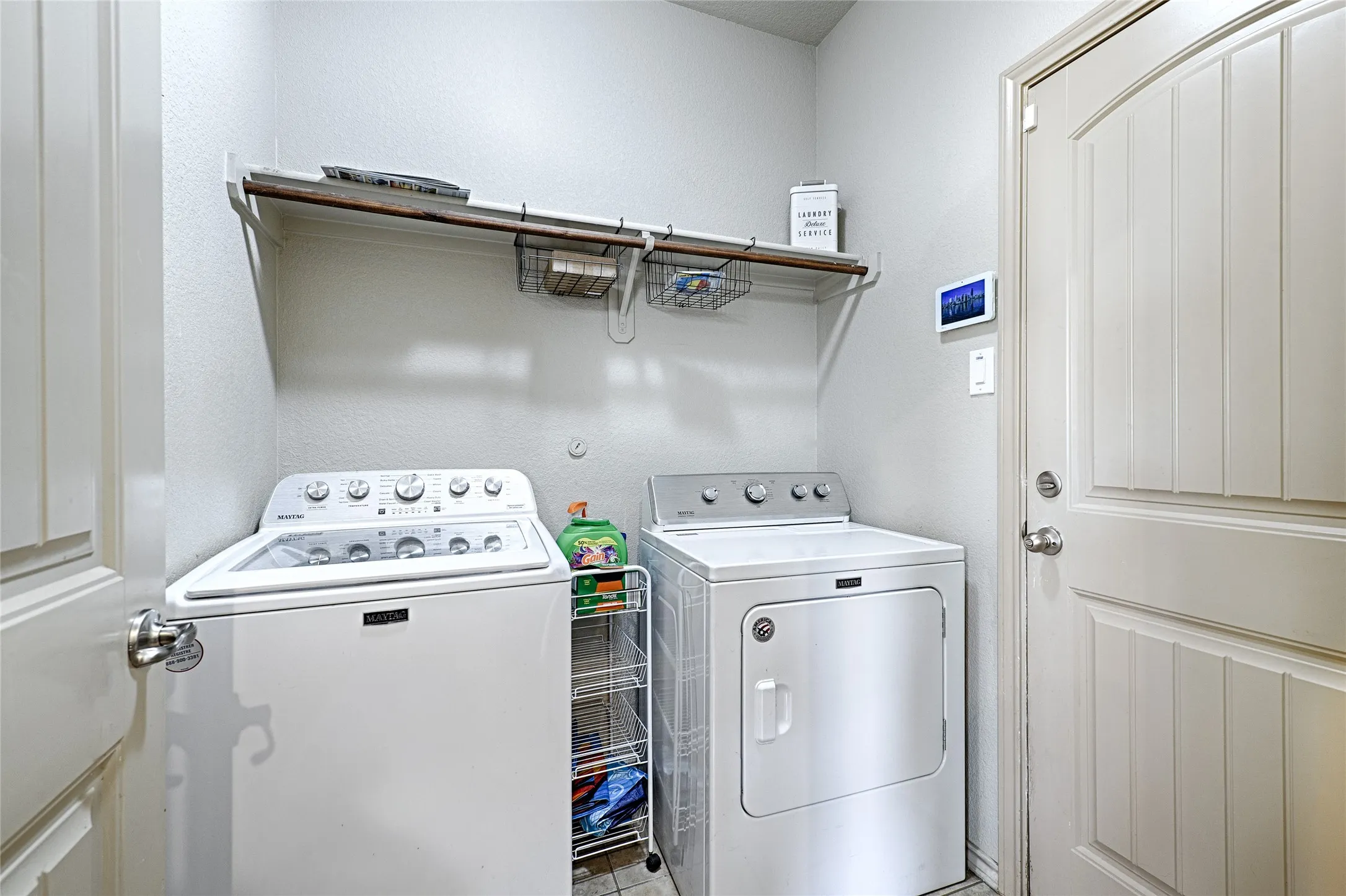 Dedicated laundry space featuring a built-in shelf, white paneled door, light gray wall paint, and tile flooring