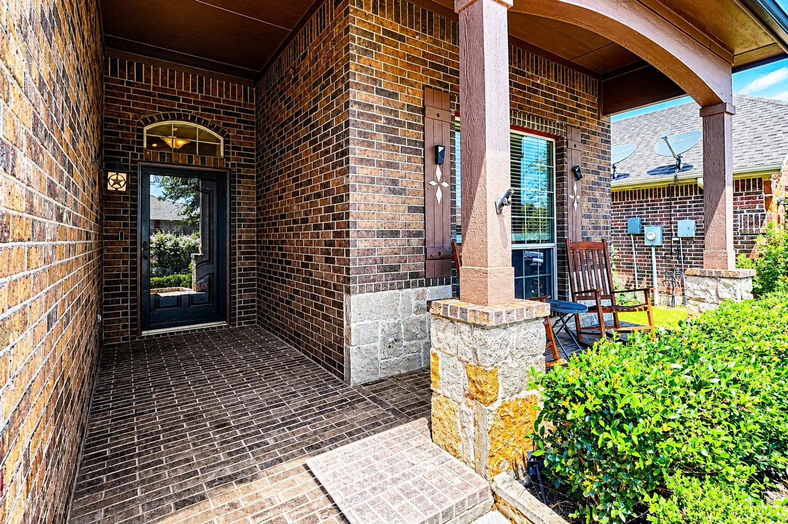 Welcoming covered entry featuring a paneled front door with an arched transom window, brick walls, and a patterned brick-finish floor