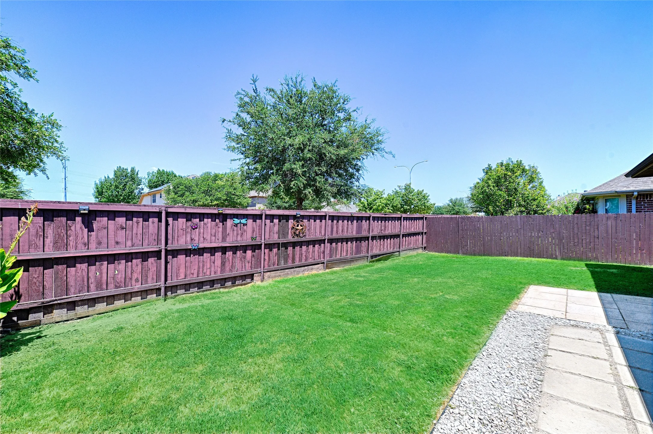 Expansive backyard featuring a manicured lawn, a full privacy fence, and a paved patio area with an adjacent gravel border