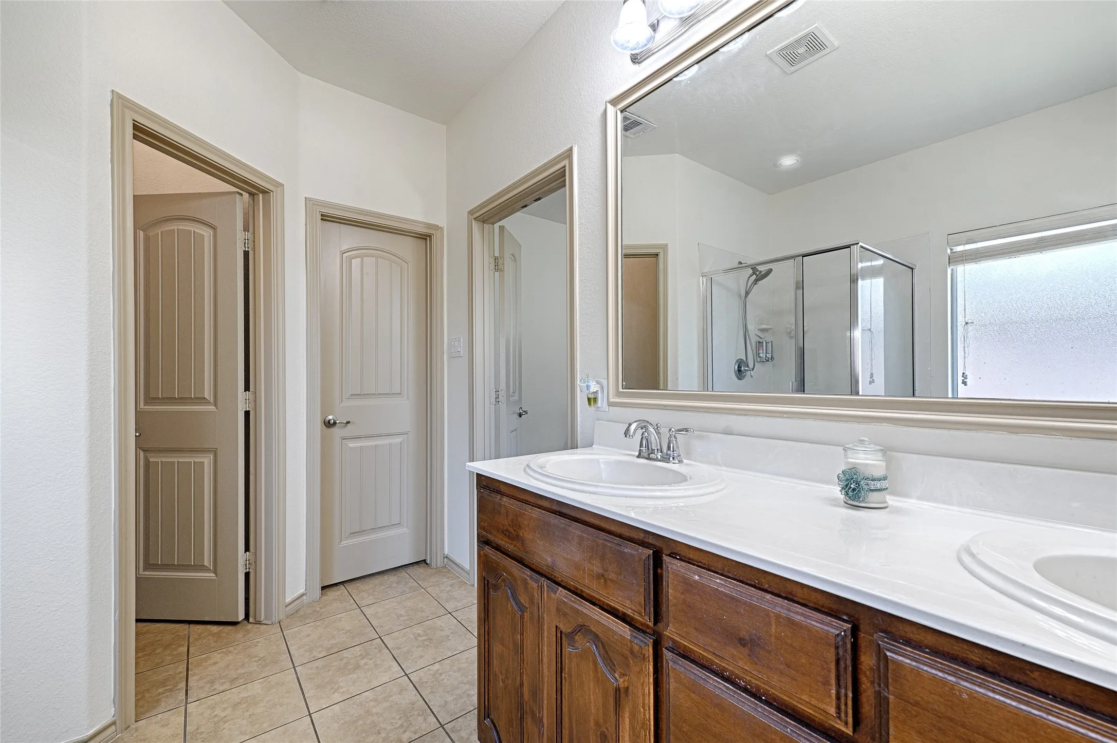 Bathroom featuring a spacious double vanity with wood cabinetry, integrated sinks, and a large framed mirror