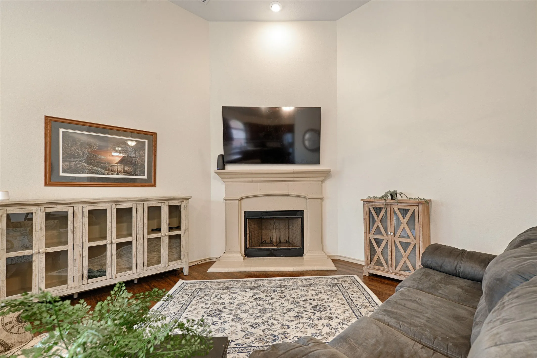 Corner fireplace with a light-toned surround and dark firebox, complemented by hardwood-finish flooring and a neutral color palette