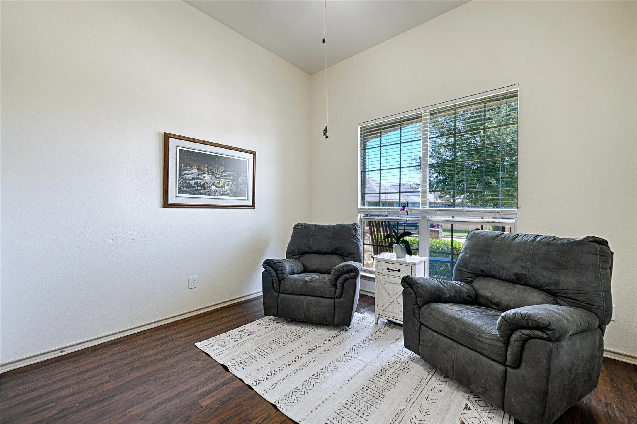 Bright interior space featuring a large window with blinds, wood-finish flooring, and vaulted ceilings
