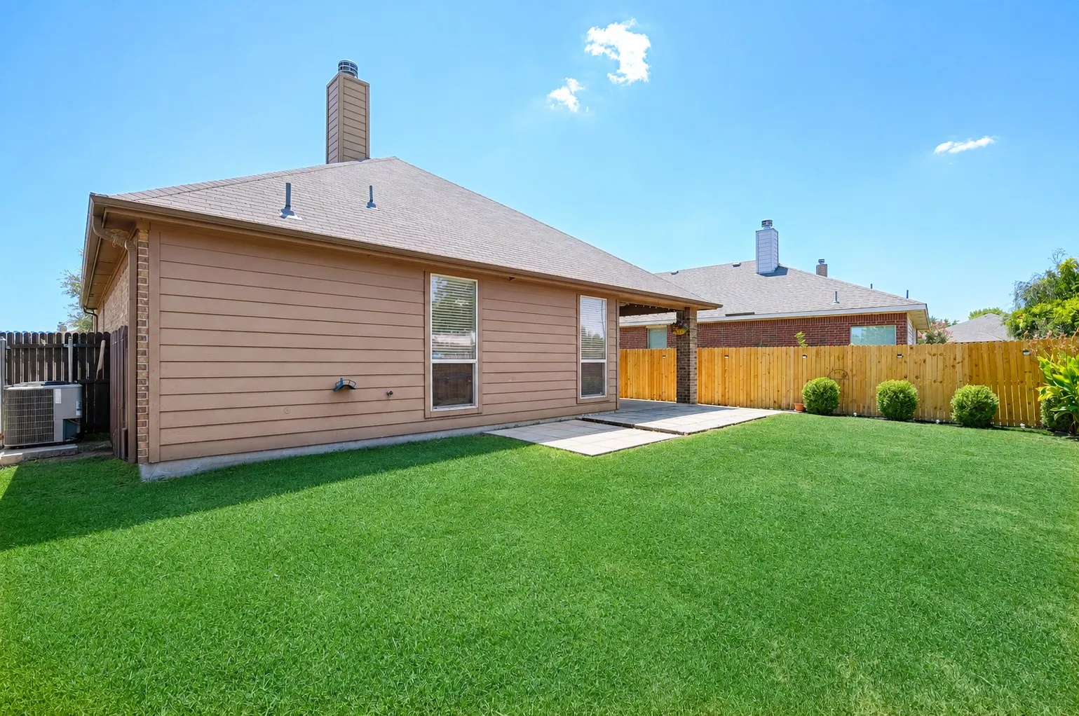 Expansive green lawn with a newly installed wood privacy fence, featuring a concrete patio and a tan siding exterior