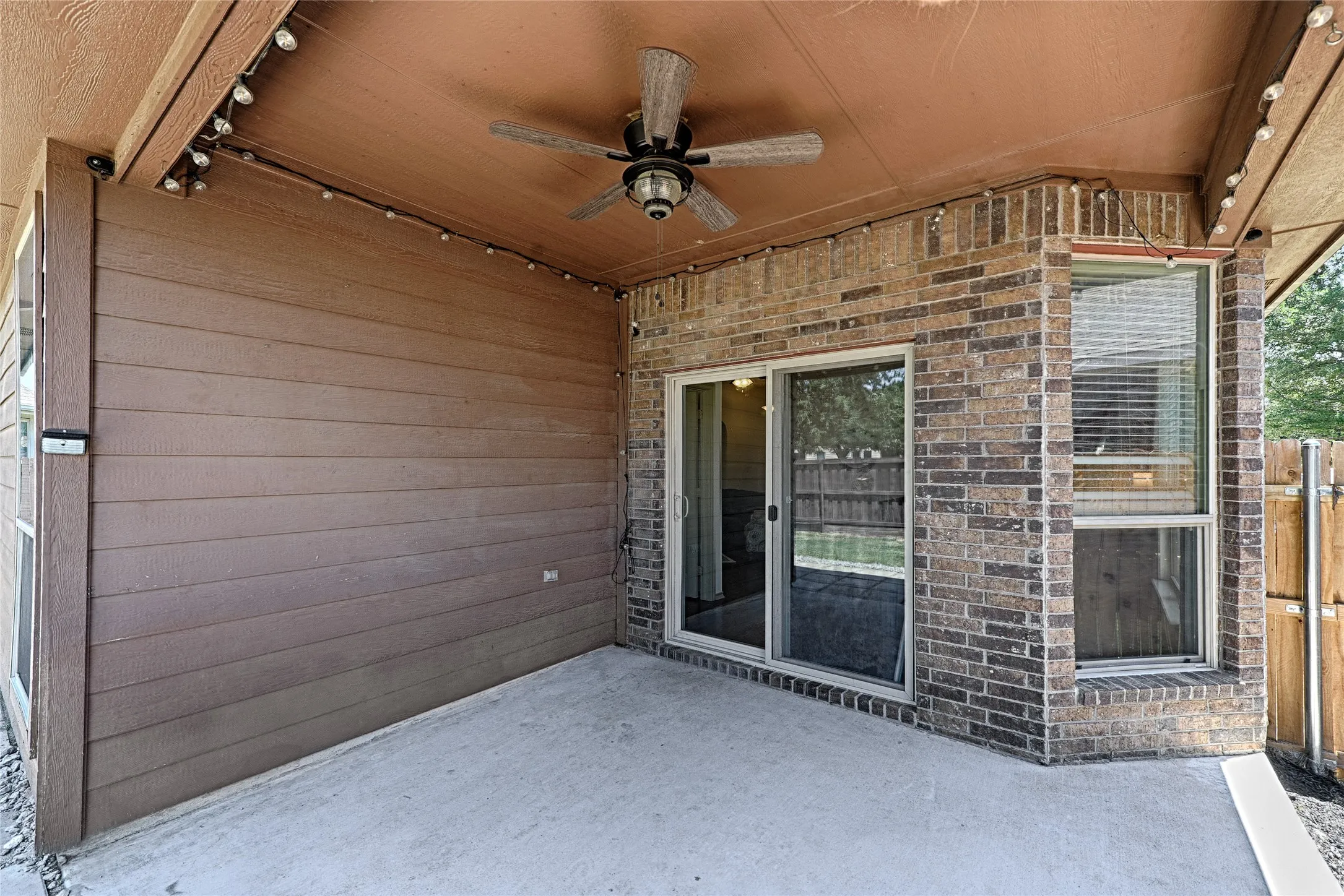 Covered concrete patio featuring a ceiling fan, string lighting, and direct access through a sliding glass door