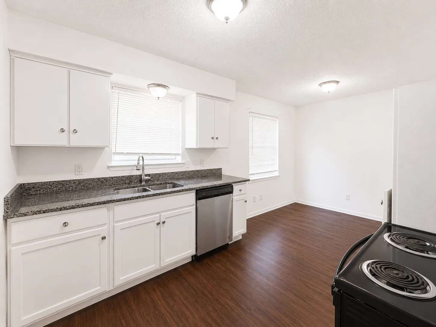 Open concept kitchen featuring white cabinetry, dark speckled countertops, and a stainless steel dishwasher