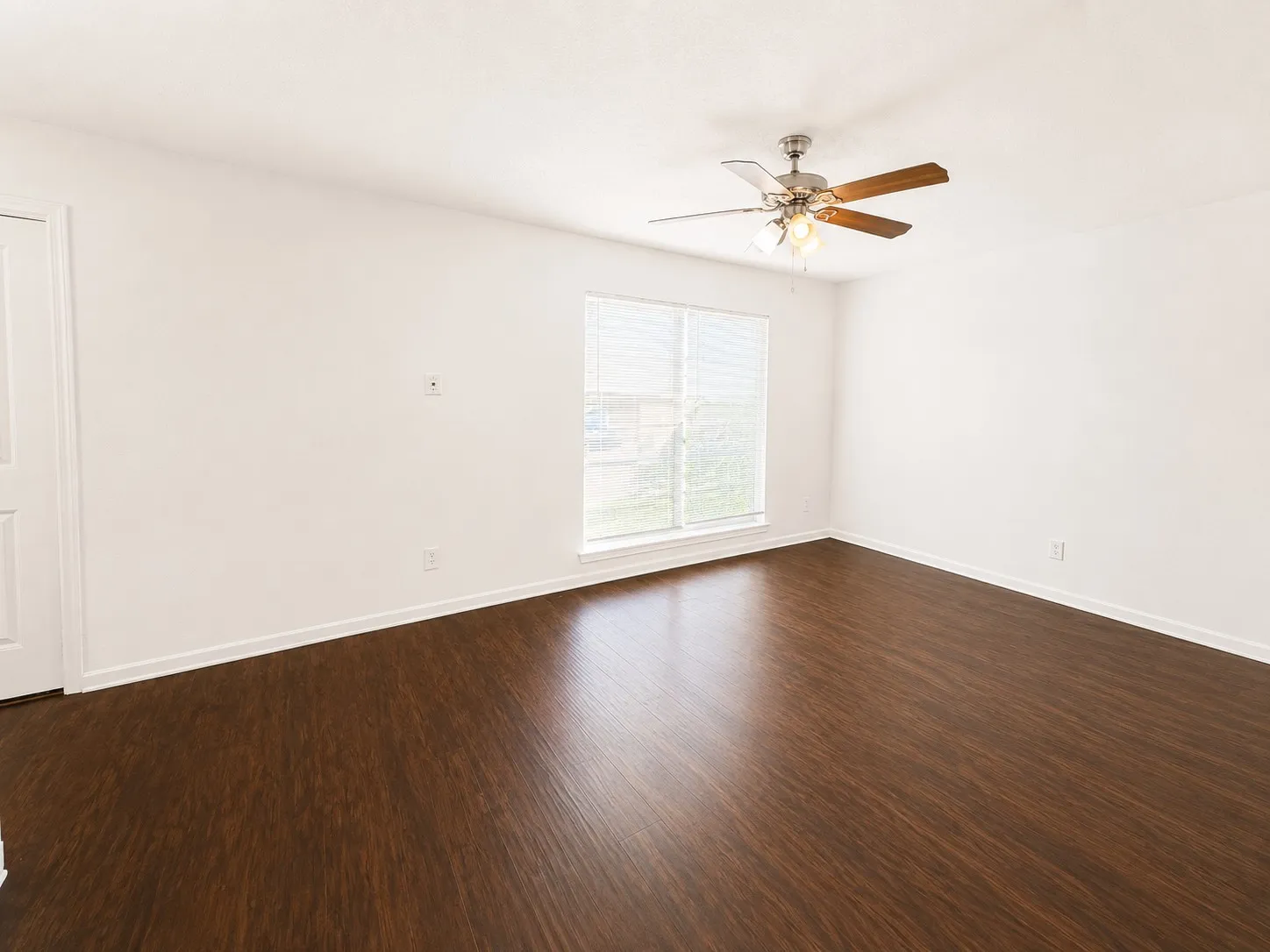 Spacious room featuring dark wood-finish flooring, white walls, and a ceiling fan with light fixture
