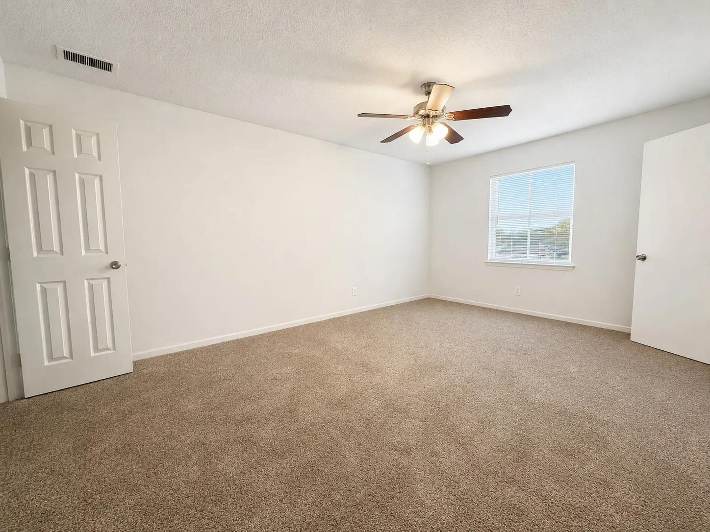 Spacious room featuring neutral carpeting, white painted walls, and a multi-speed ceiling fan with TWO closets