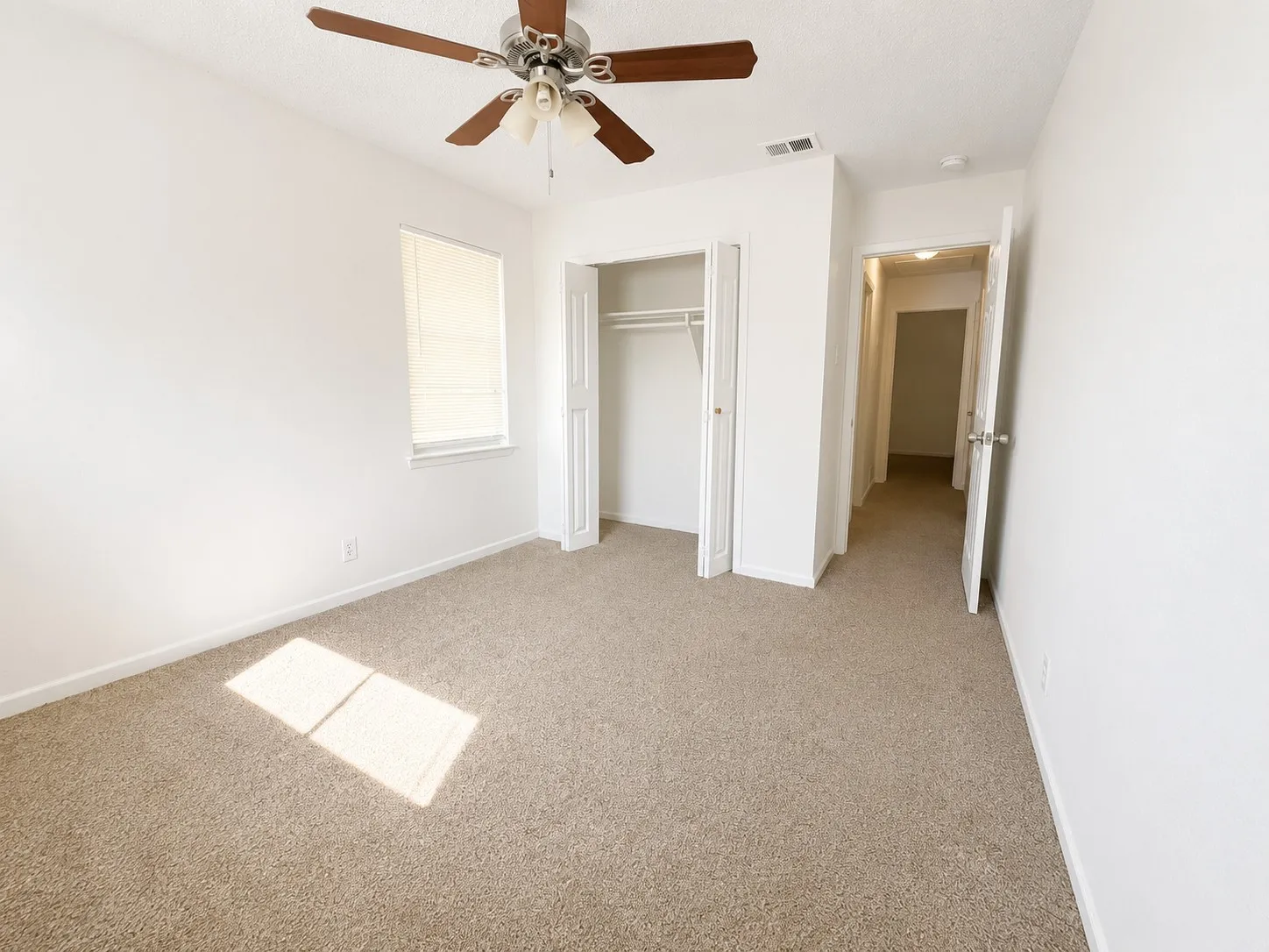 Carpeted interior room with a ceiling fan light fixture, a window with blinds, and a bi-fold closet