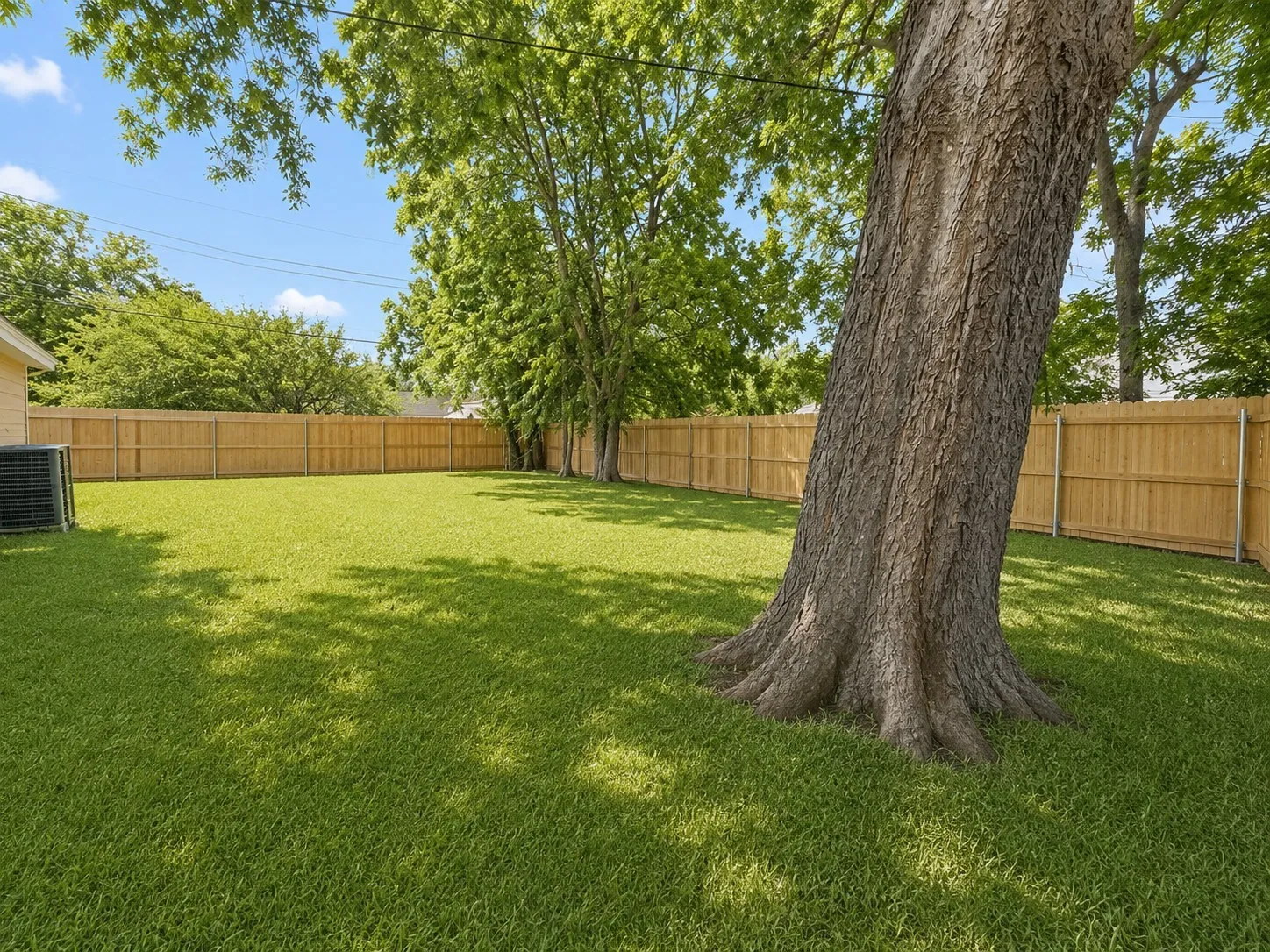 Expansive green lawn with mature shade trees, full privacy fencing.