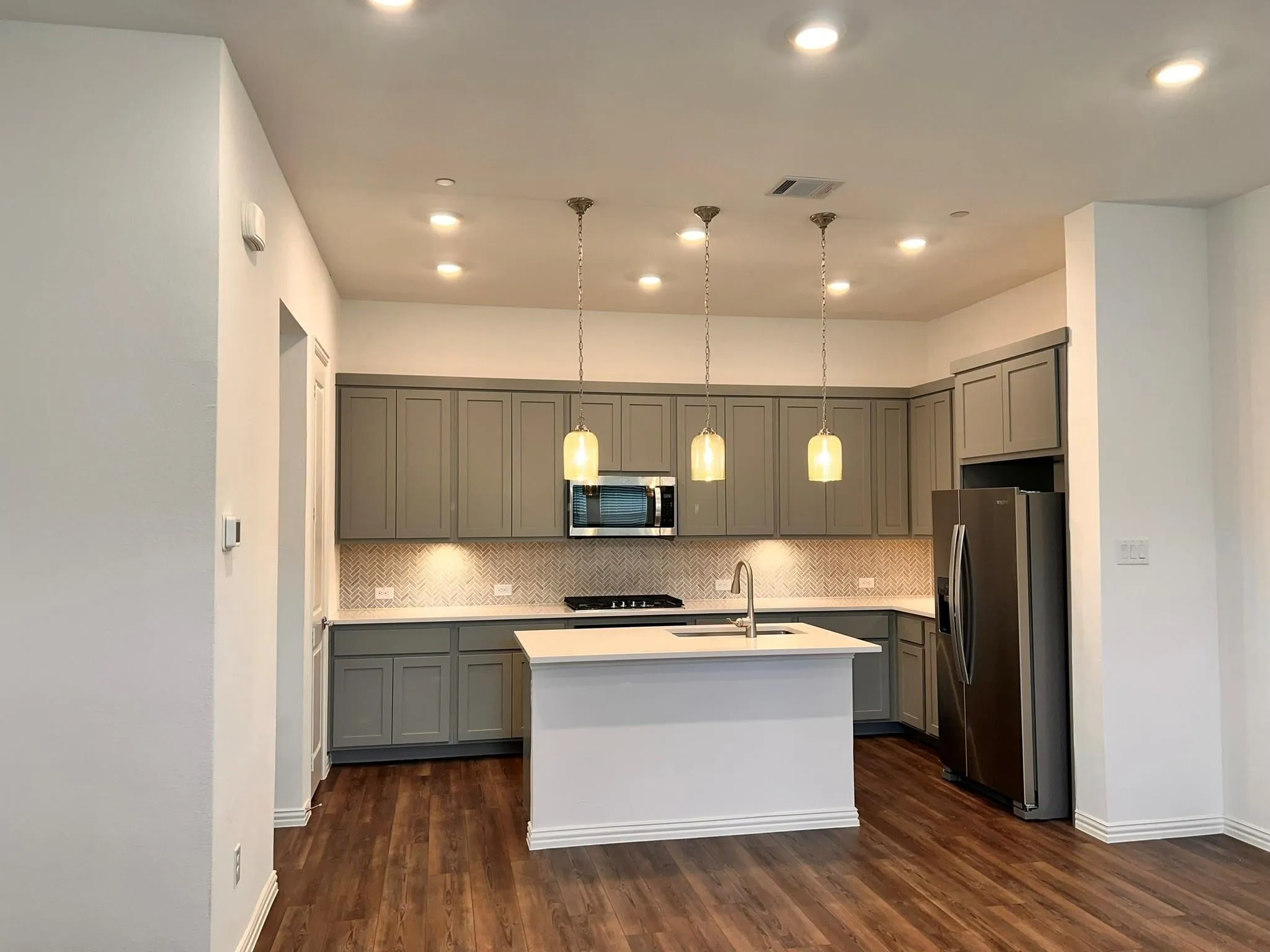 Contemporary kitchen featuring gray shaker-style cabinetry, a white island with an undermount sink, and stainless steel appliances