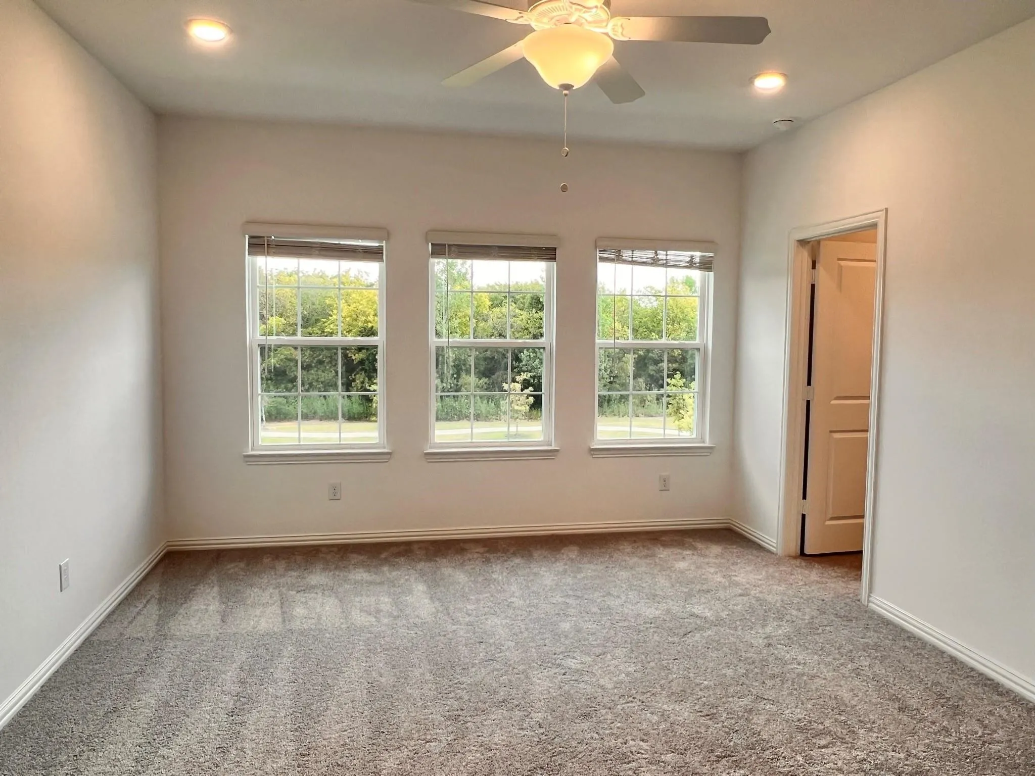 Carpeted room featuring three windows with blinds, recessed lighting, and a ceiling fan with integrated light fixture
