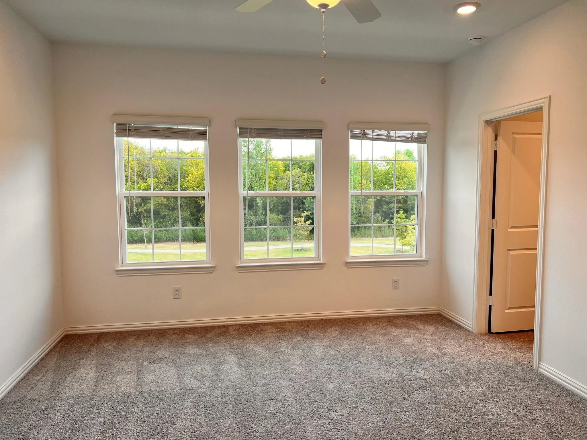 Bright room featuring three double-hung windows, recessed ceiling lighting, a ceiling fan, plush carpet flooring, and white trim