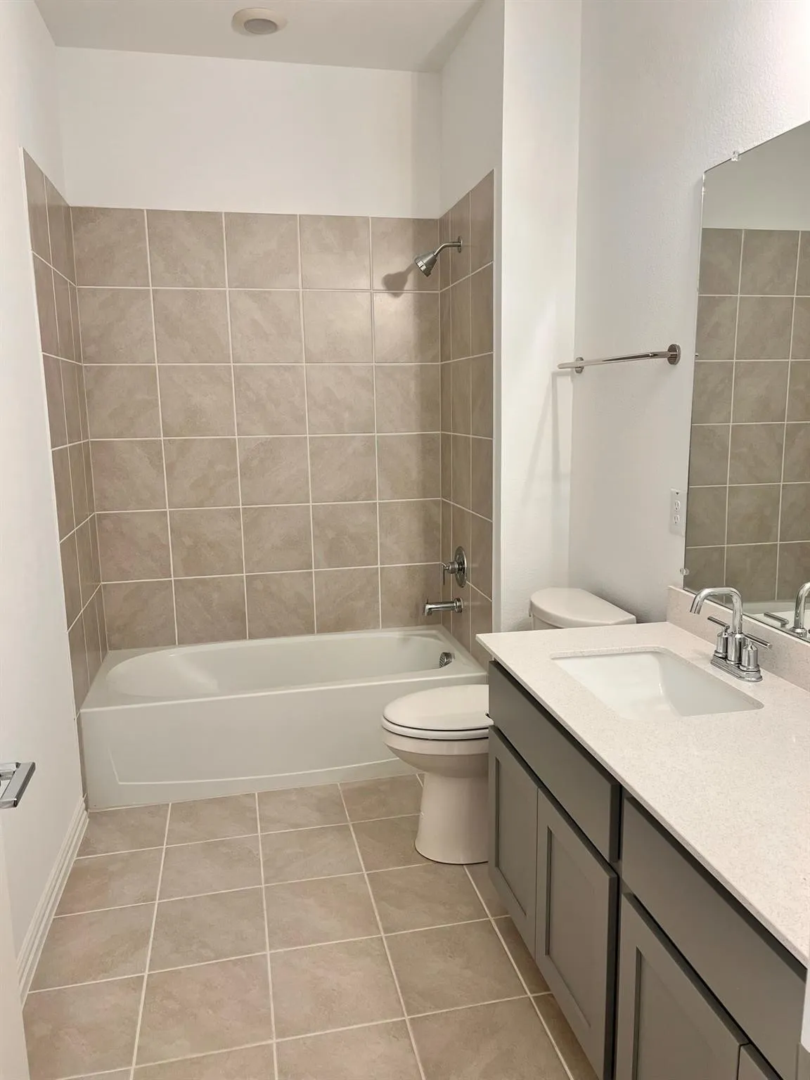 Bathroom featuring a full-size tub with tile surround, a built-in vanity with light-toned countertop and undermount sink, and tiled flooring